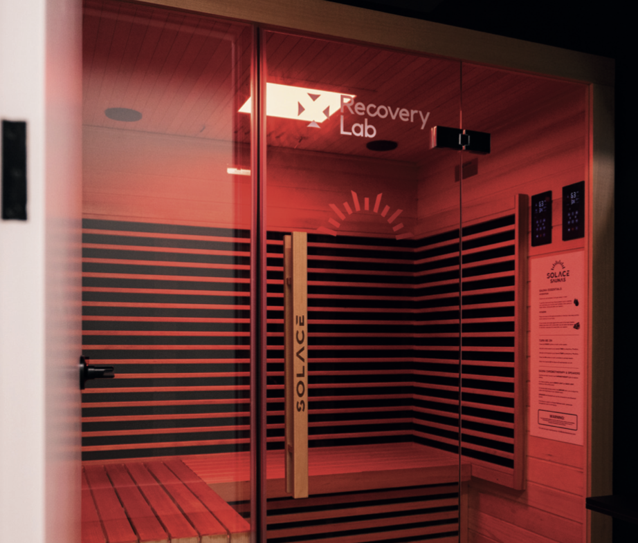 An infrared sauna with glass doors labeled 'Solace' and 'Recovery Lab' with wood paneling and internal digital control panels.