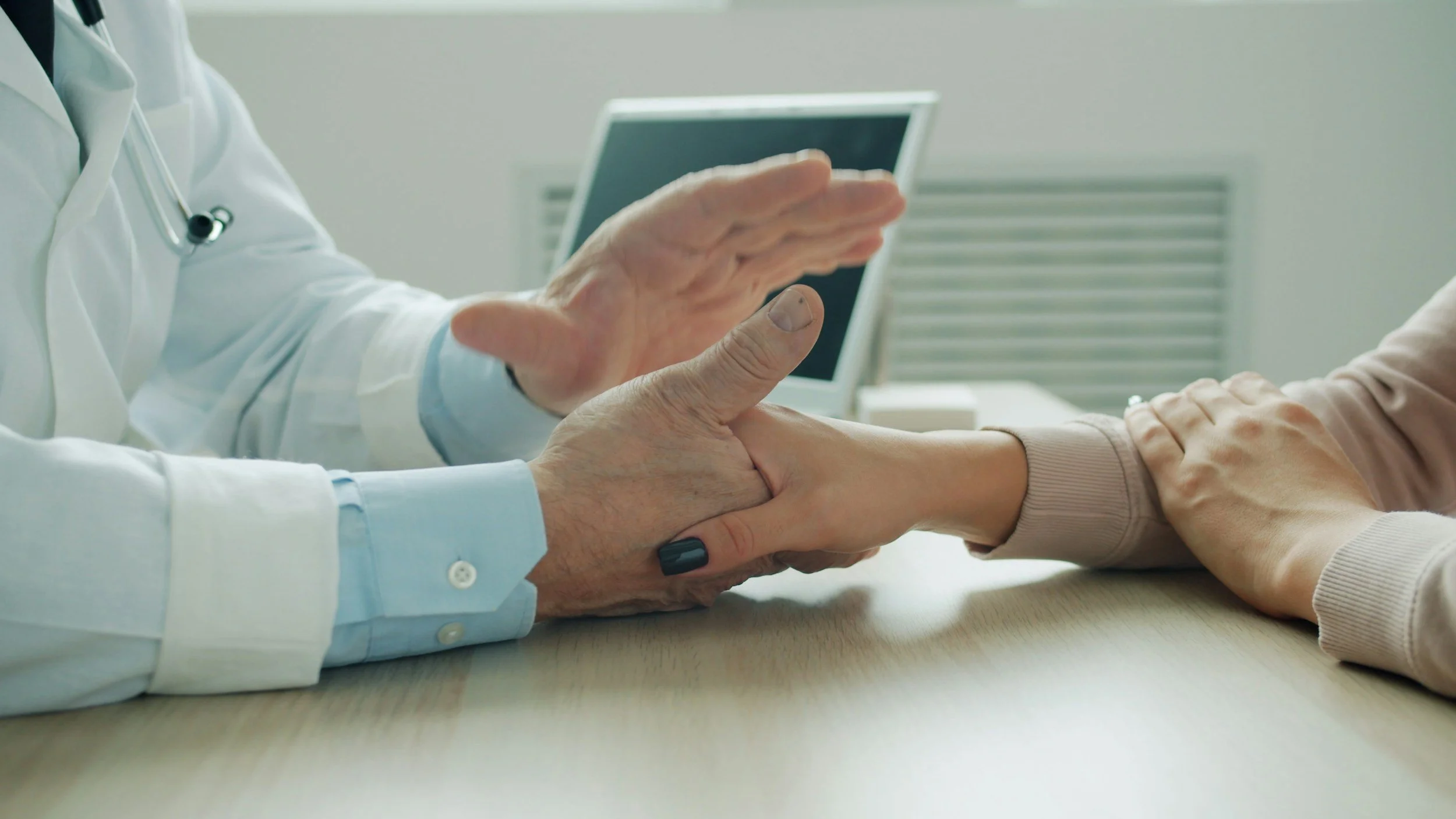 A doctor holding a patient's hand in a comforting gesture at a medical consultation.