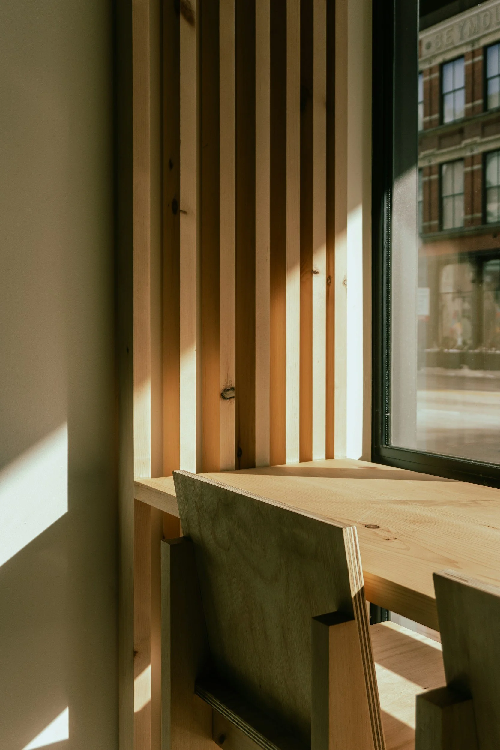 Sunlight streaming through a window illuminating a wooden wall with vertical slats, a wooden table, and a chair.