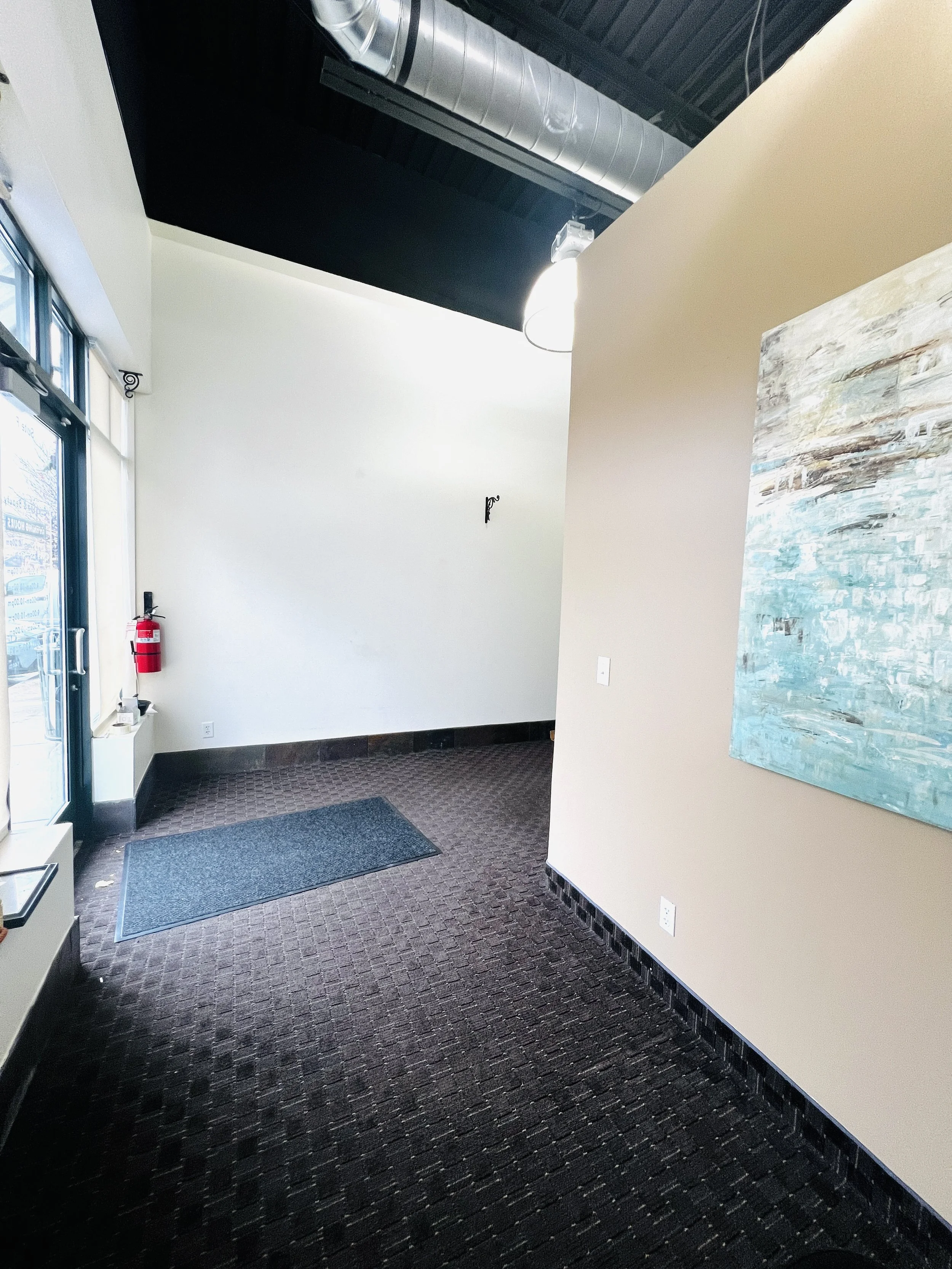 Living room with two white armchairs, a small round table with a vase and dried branches, a large window with a mural of a woman sleeping, and a potted plant, illuminated by wall sconce and hanging lights.