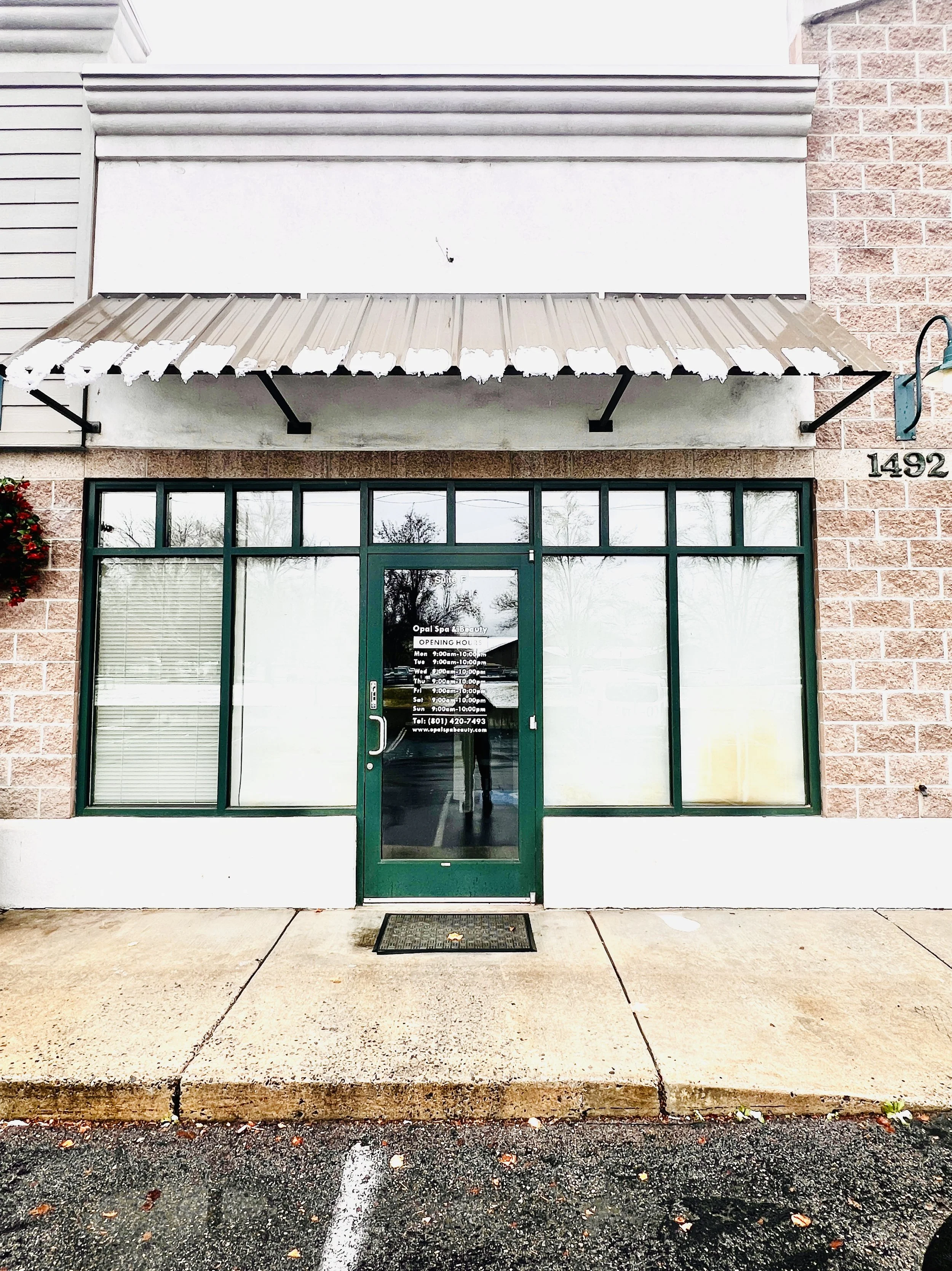 The storefront of a massage therapy clinic with large windows displaying images of people receiving massages and a neon 'OPEN' sign. The door has a sign that reads 'Suite A' and a message about safety and mask-wearing.