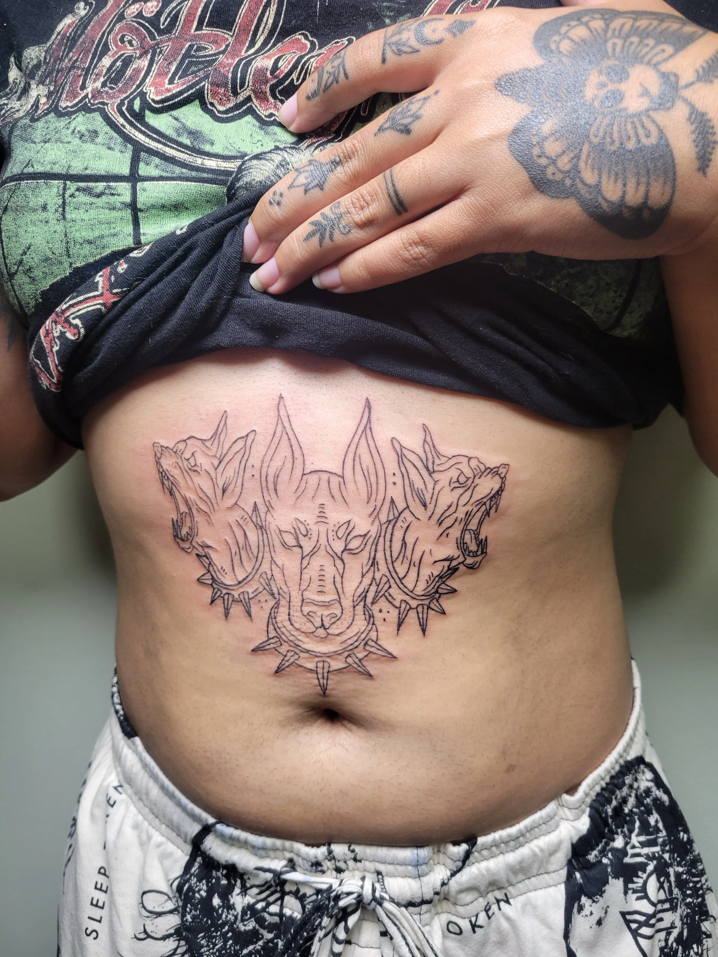 A person's midsection showing a fresh, detailed tattoo of three wolf heads on the lower abdomen.
