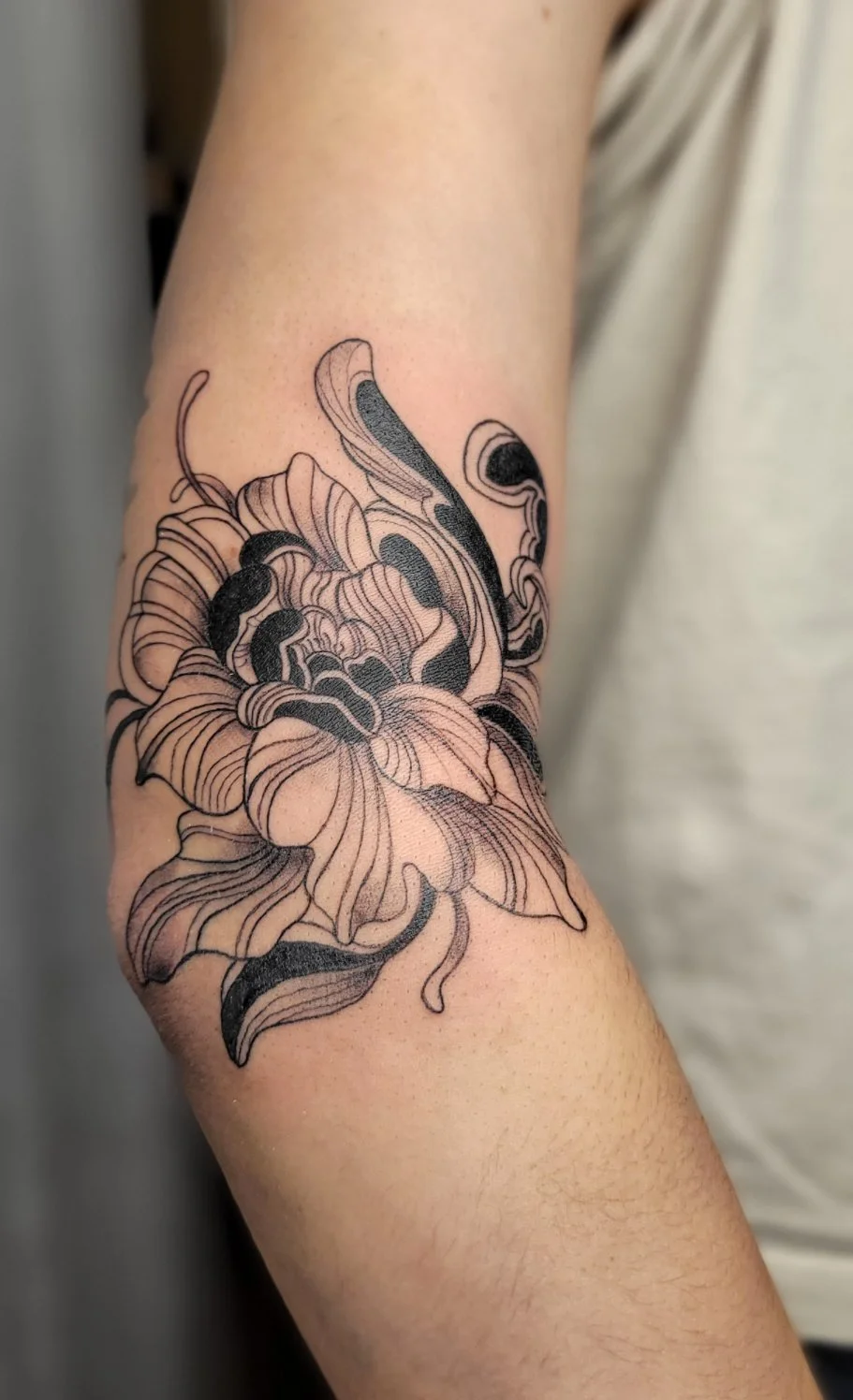 Black and gray tattoo of a large, detailed flower on a person's arm.