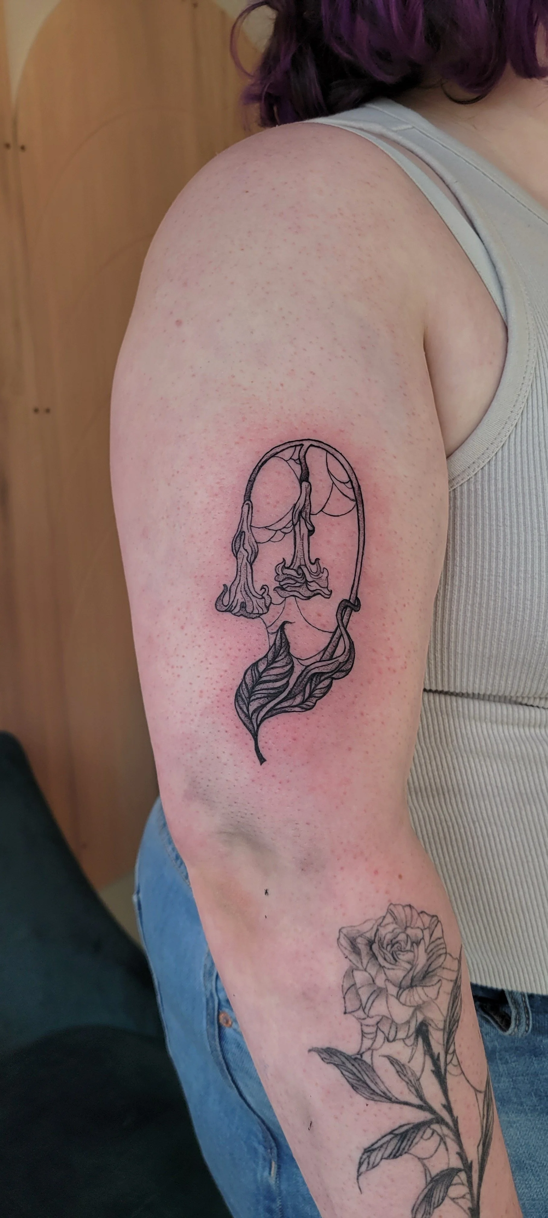 Tattoo of a face outline with feminine features and flowing hair, with a leaf at the bottom, on a woman's upper arm.