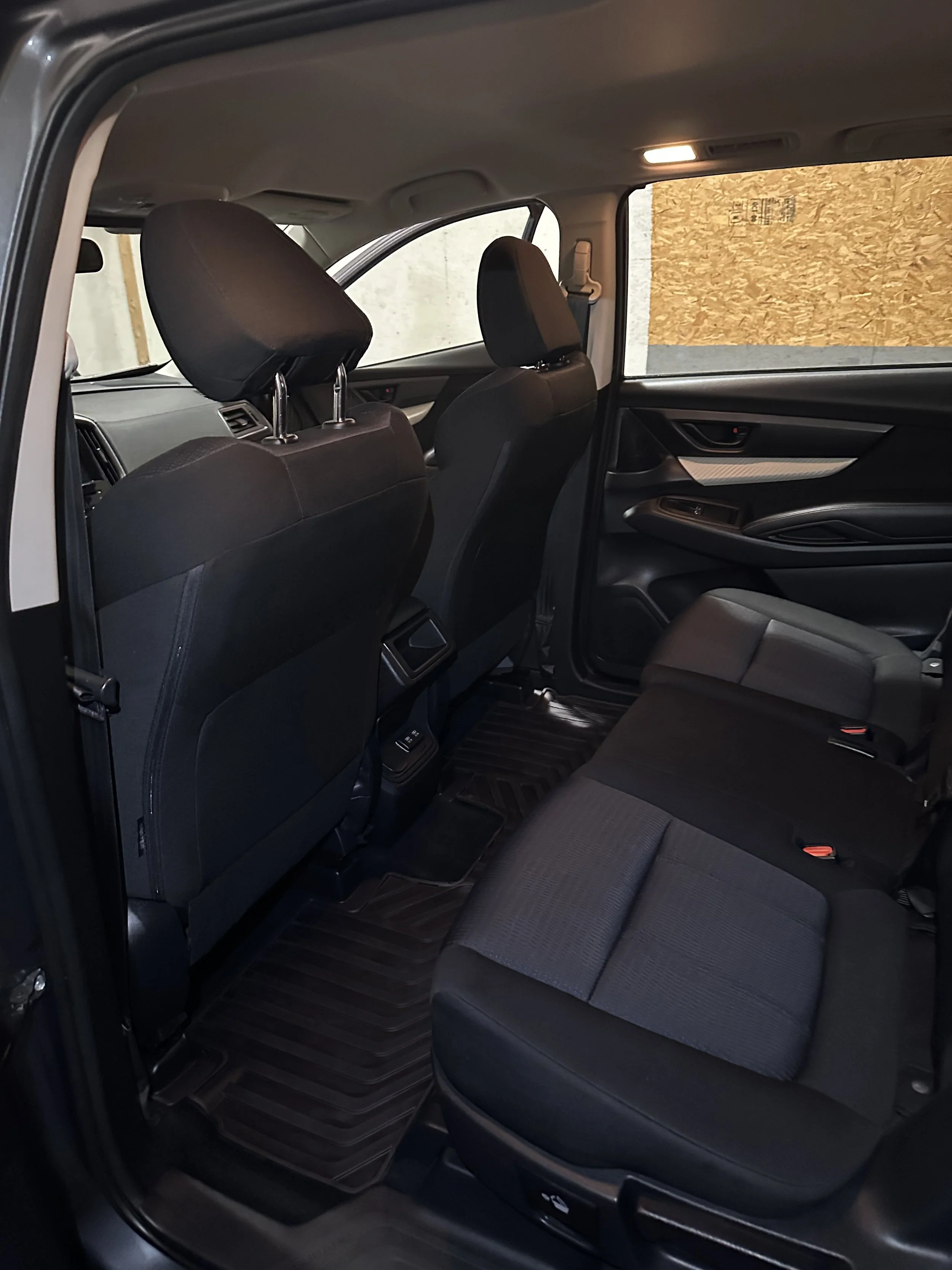 Interior of a vehicle showing the clean backseat area with black seats, floor mats, and rear of the front seats with headrests.
