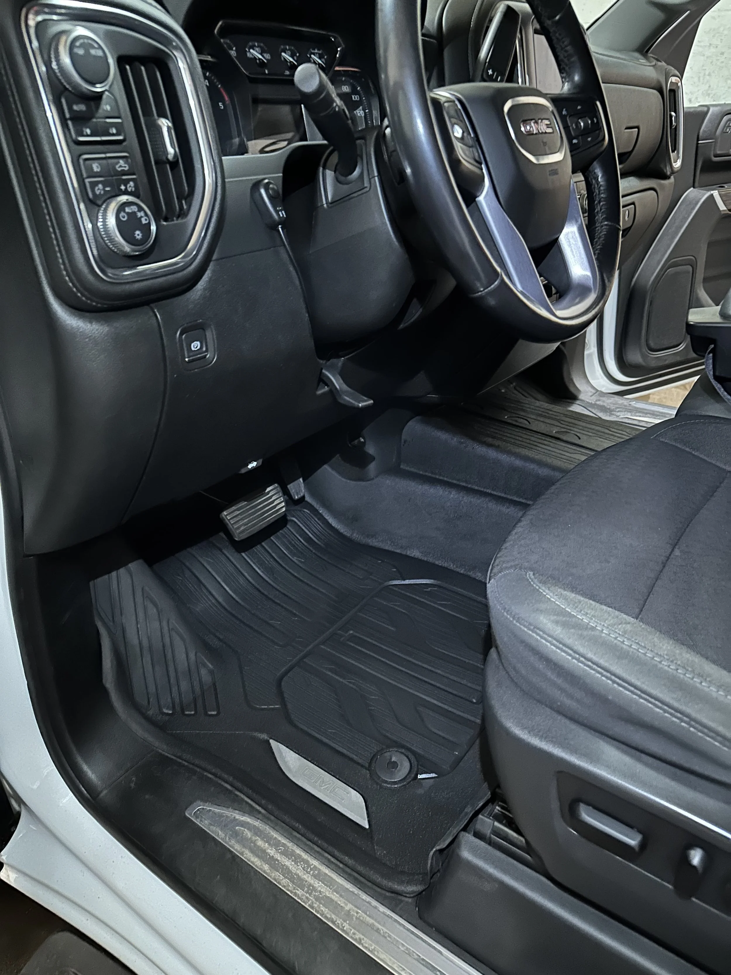 Clean detailed Interior of a GMC vehicle showing the driver's side dashboard, steering wheel, gas pedal, and floor mat.