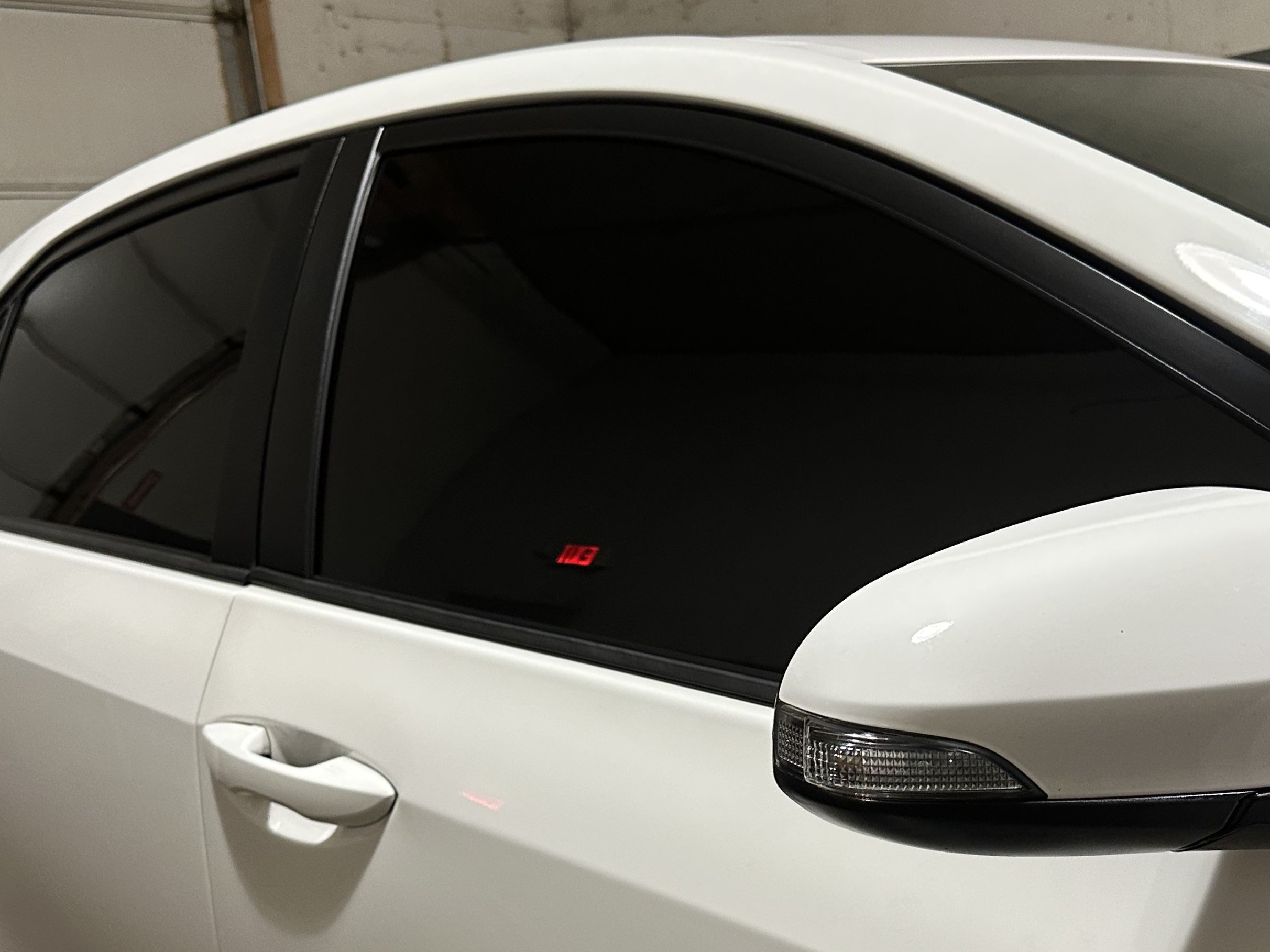 Close-up of a clean white car's passenger side, showing the rear passenger door, and black tinted windows.
