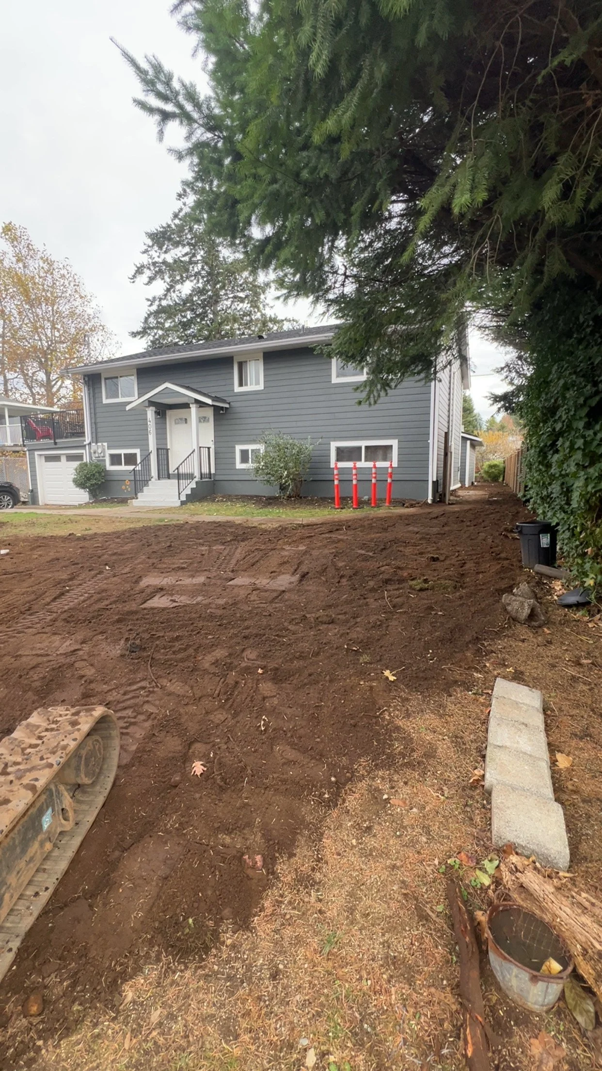 A house with blue siding and white trim, surrounded by a yard that is under renovation with bare soil and construction materials nearby.