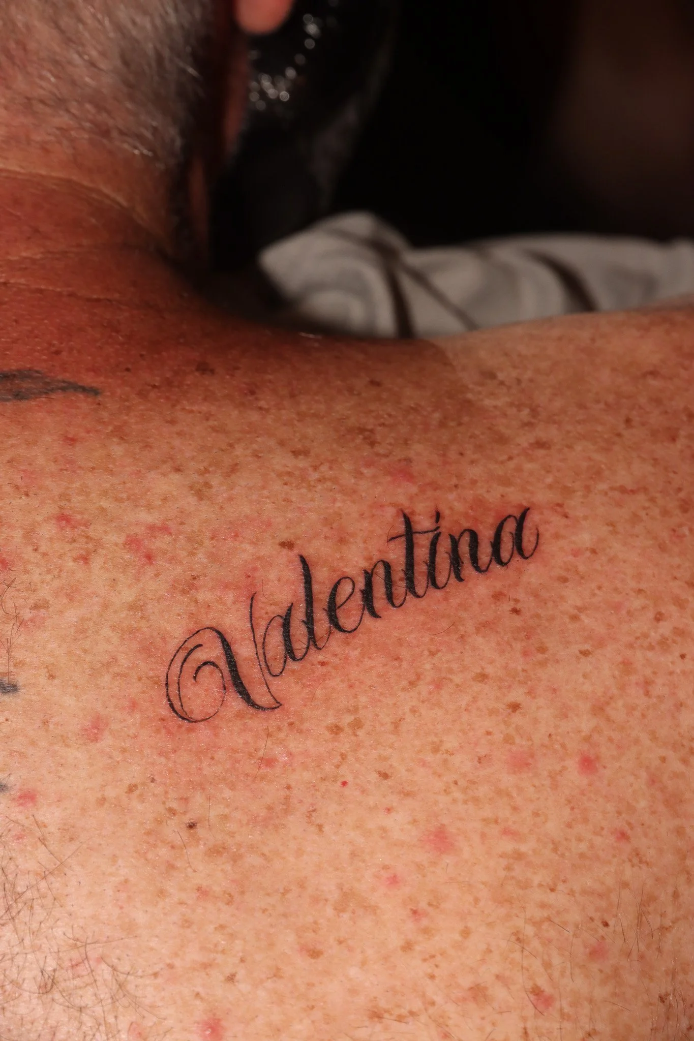 Close-up of a person's shoulder with a tattoo that reads '@adentina' in cursive script.