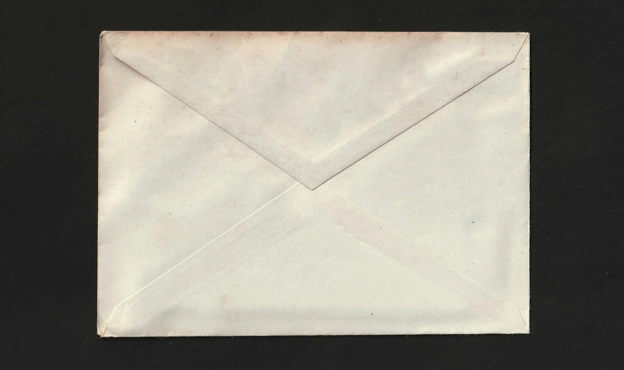 A plain white envelope with a triangular flap on a black surface.
