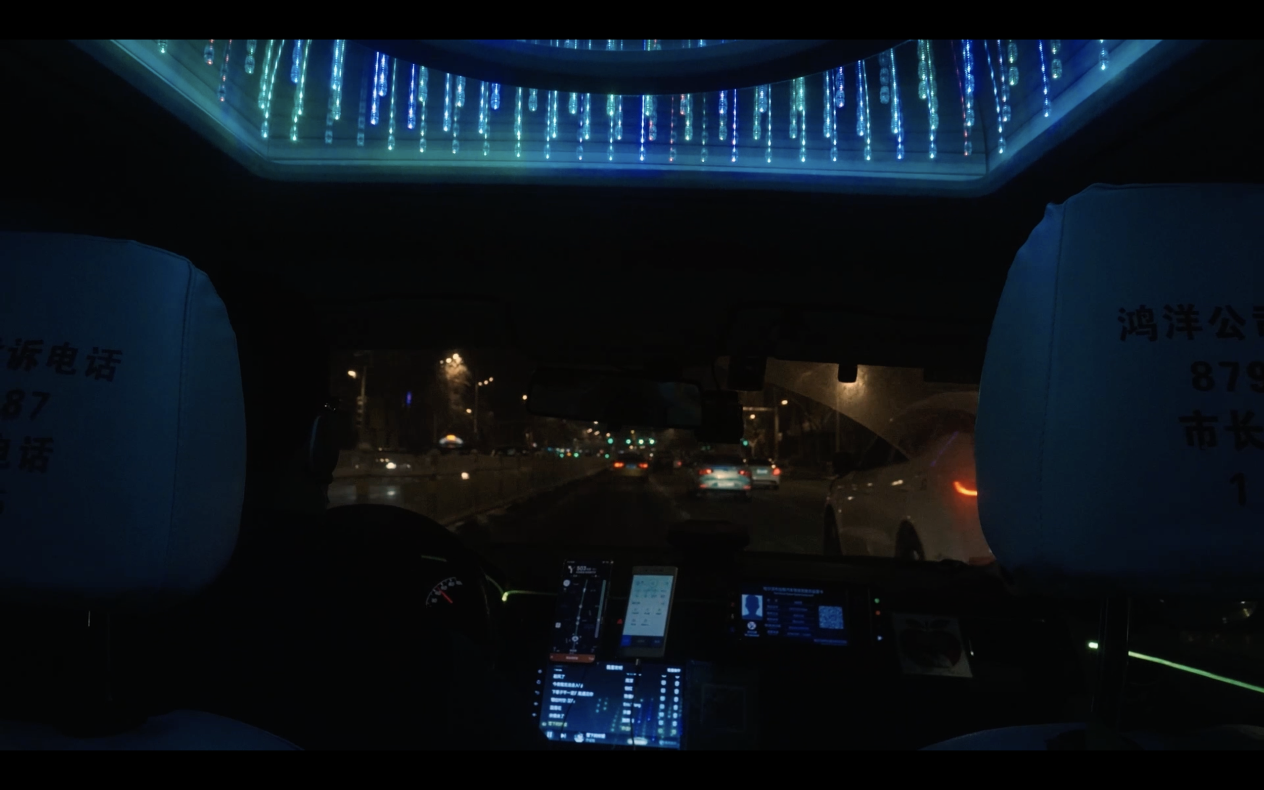 Inside a vehicle at night, showing the dashboard, rearview mirror, and illuminated decorative lights on the ceiling.