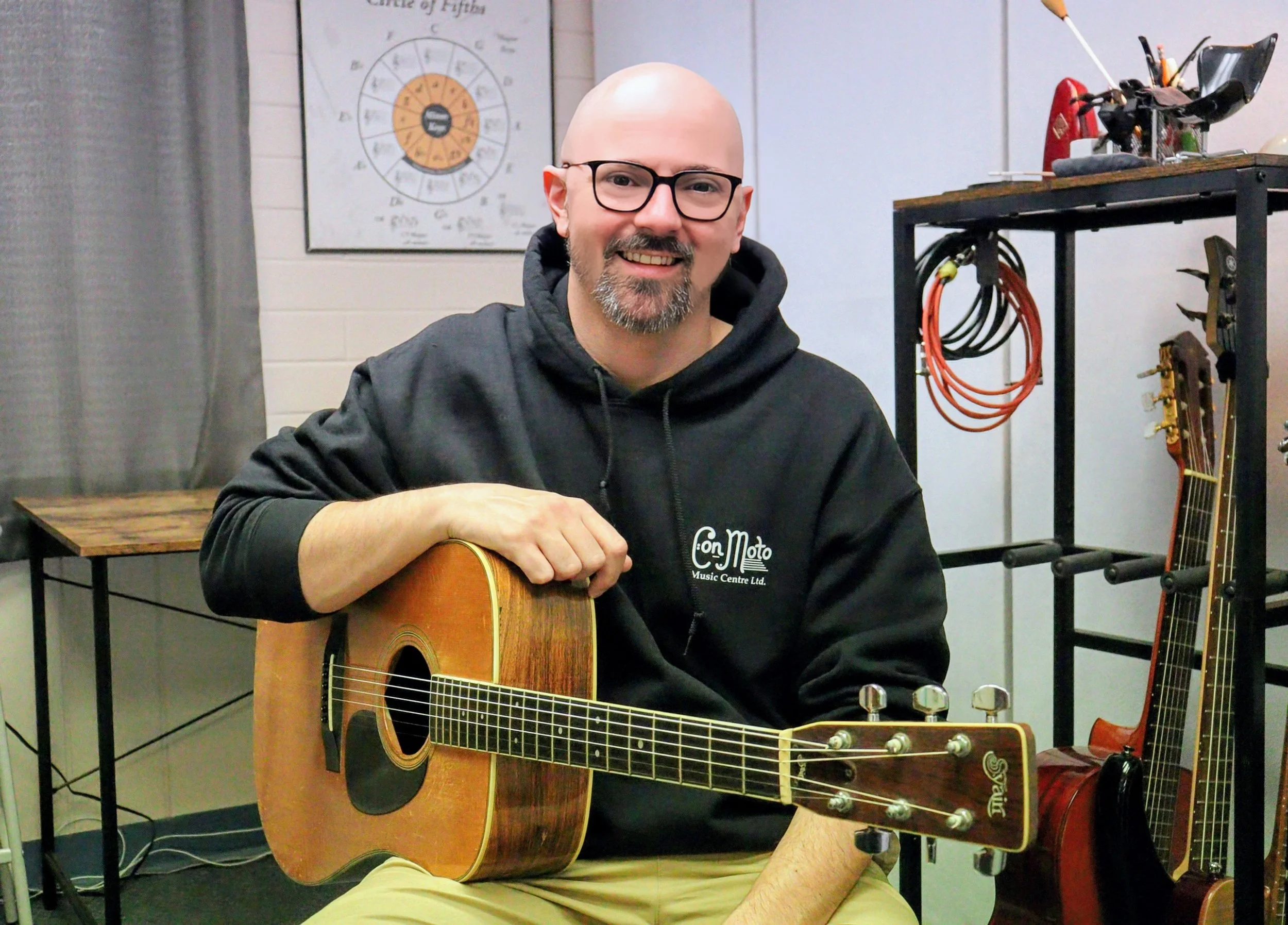 Adam Willey, a bald man with beard in dress shirt holding a double bass and bow, standing against a plain light-coloured background.