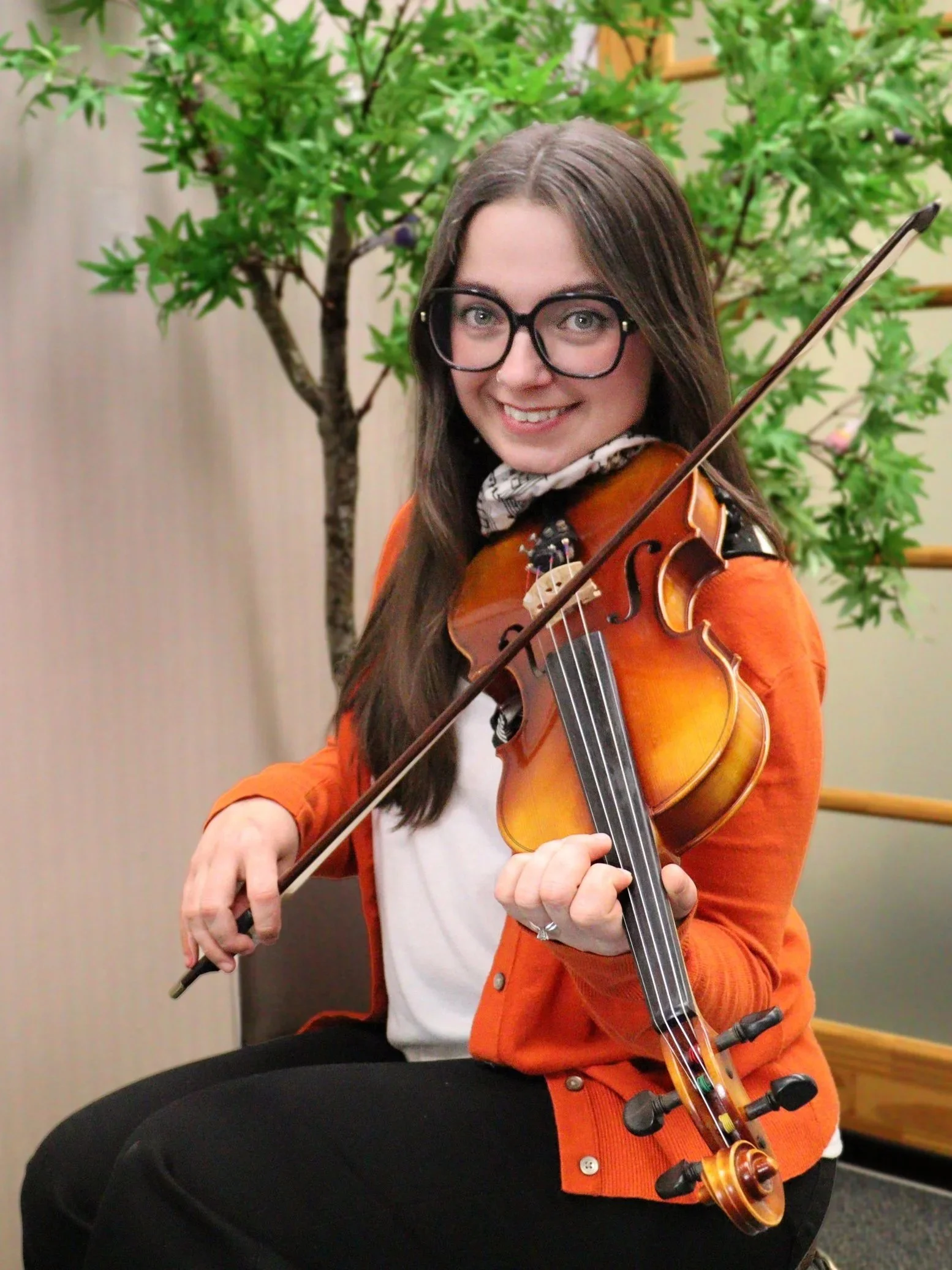 Valerie Willey, a woman with long dark hair smiling and holding a violin, standing against a plain light-coloured background.