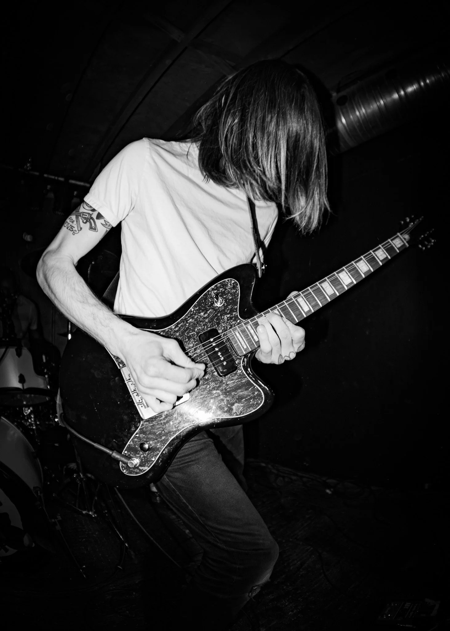 A person with long hair playing an electric guitar on stage in a dimly lit setting.