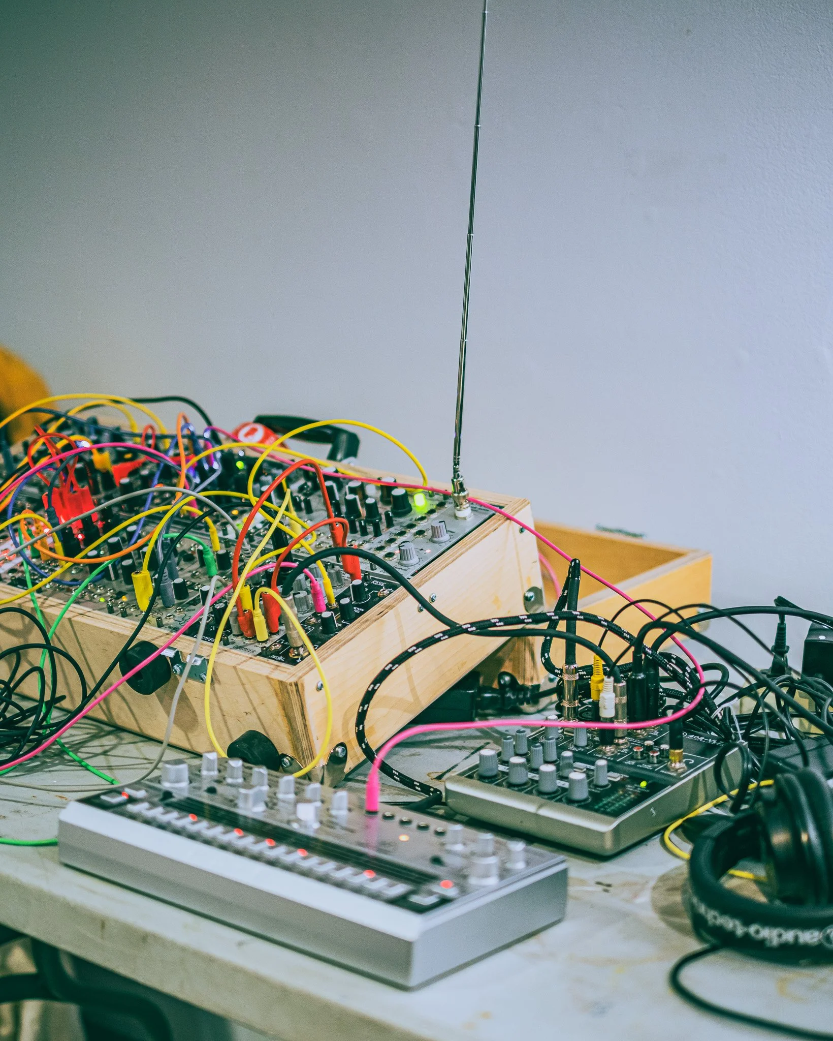 Electronic music equipment setup including a wooden modular synthesizer, a small MIDI controller, and headphones on a cluttered table.