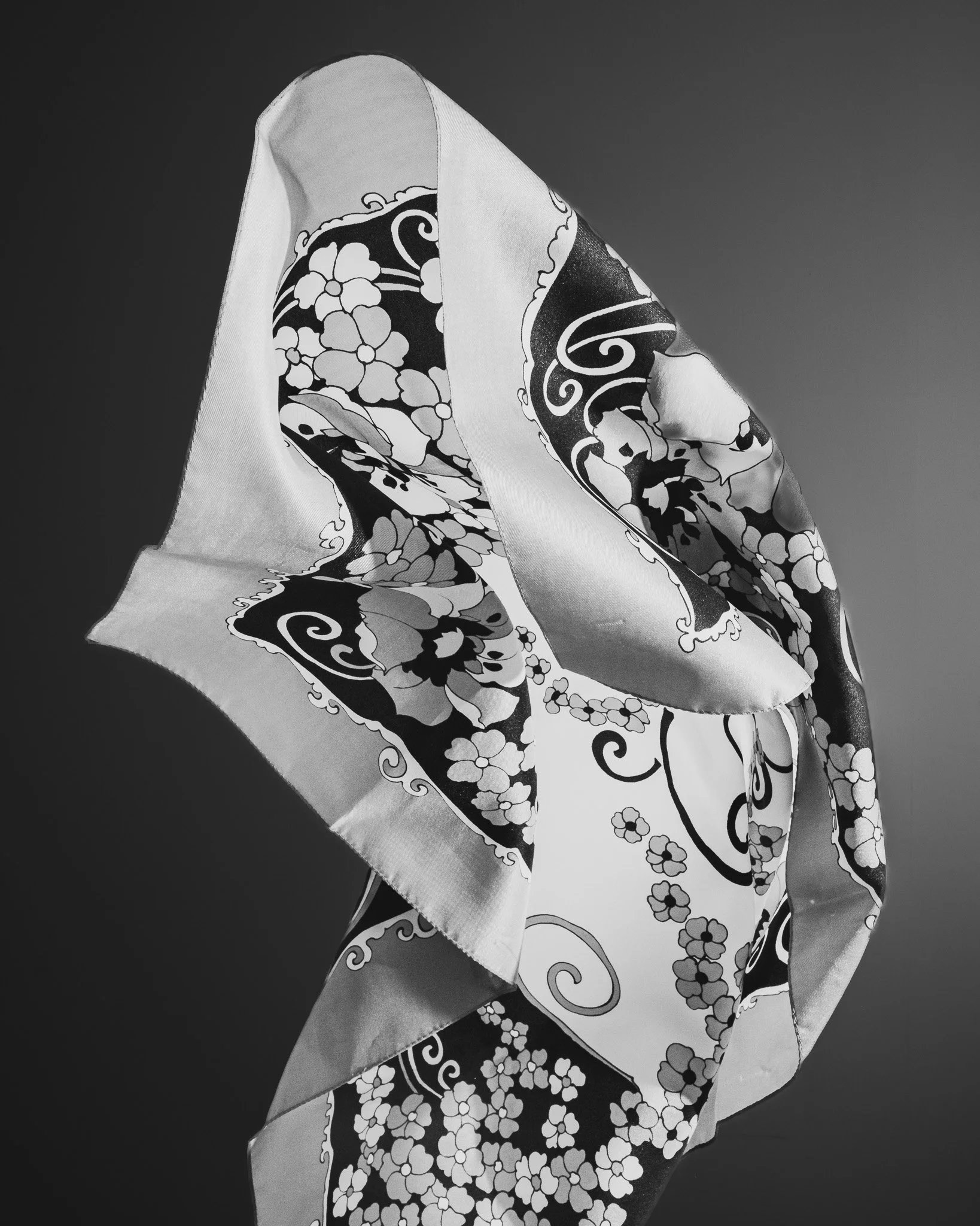 A patterned cloth, possibly a scarf or handkerchief, draped and folded against a plain background.