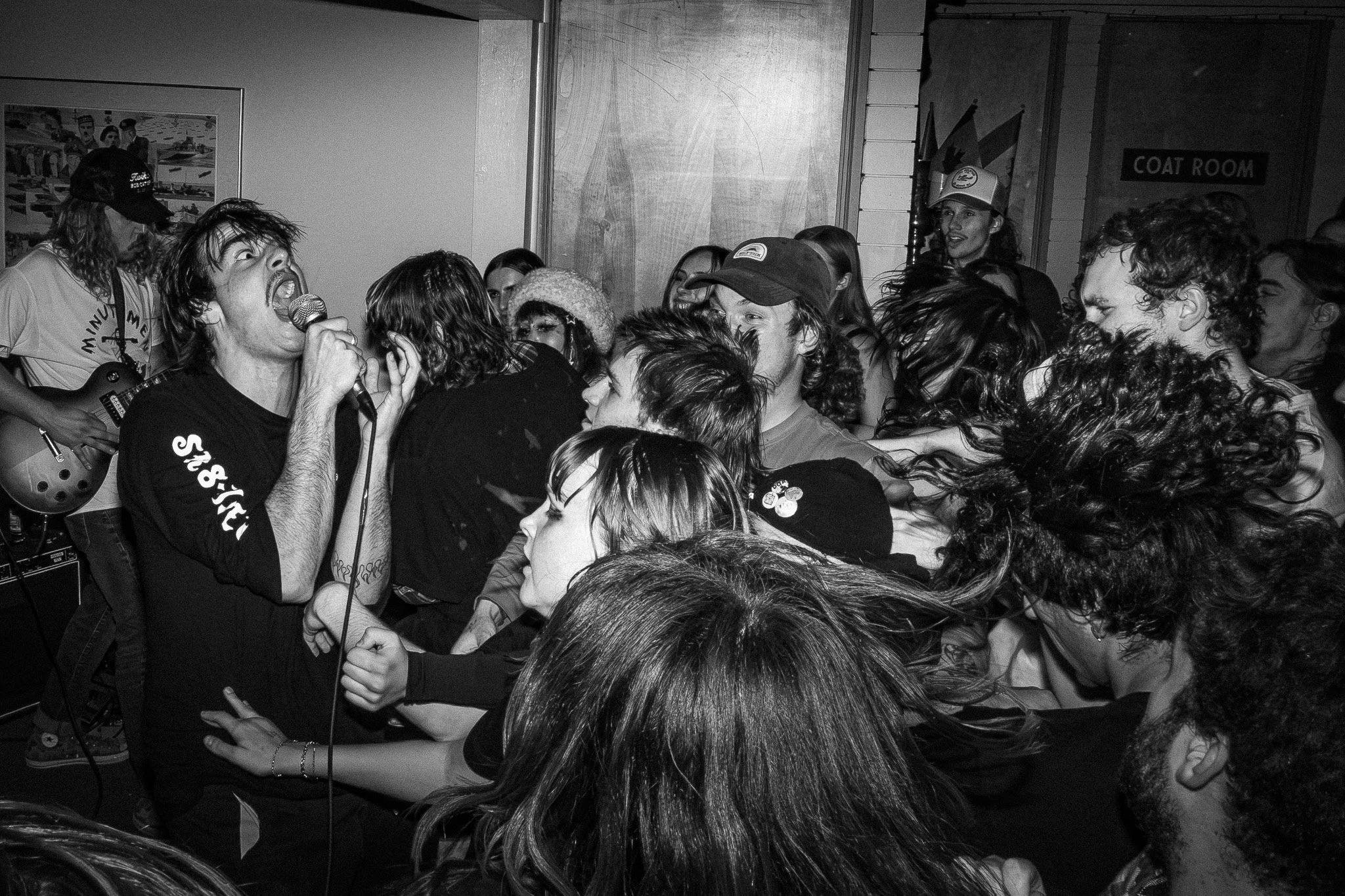 A black and white photo of a live music concert with a singer passionately performing, surrounded by a crowded audience in close proximity, with some audience members reaching toward the singer.