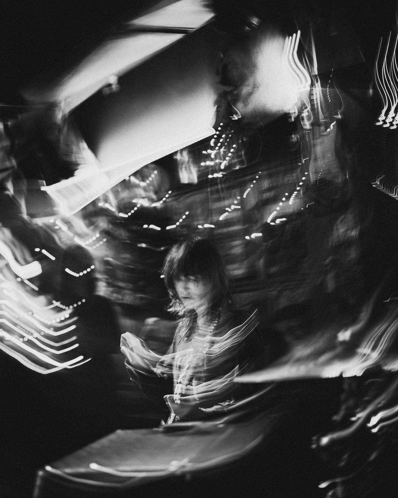 A black and white photo showing a woman with medium-length hair looking at her phone, with surrounding lights creating streaks and a sense of motion.