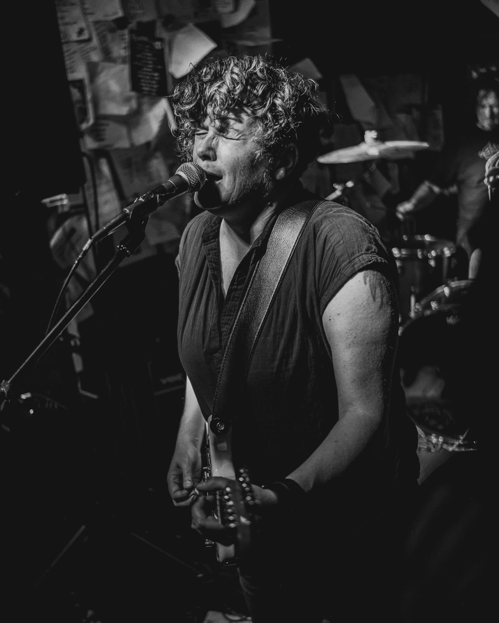 A musician passionately singing into a microphone while playing an electric guitar in a dimly lit venue.