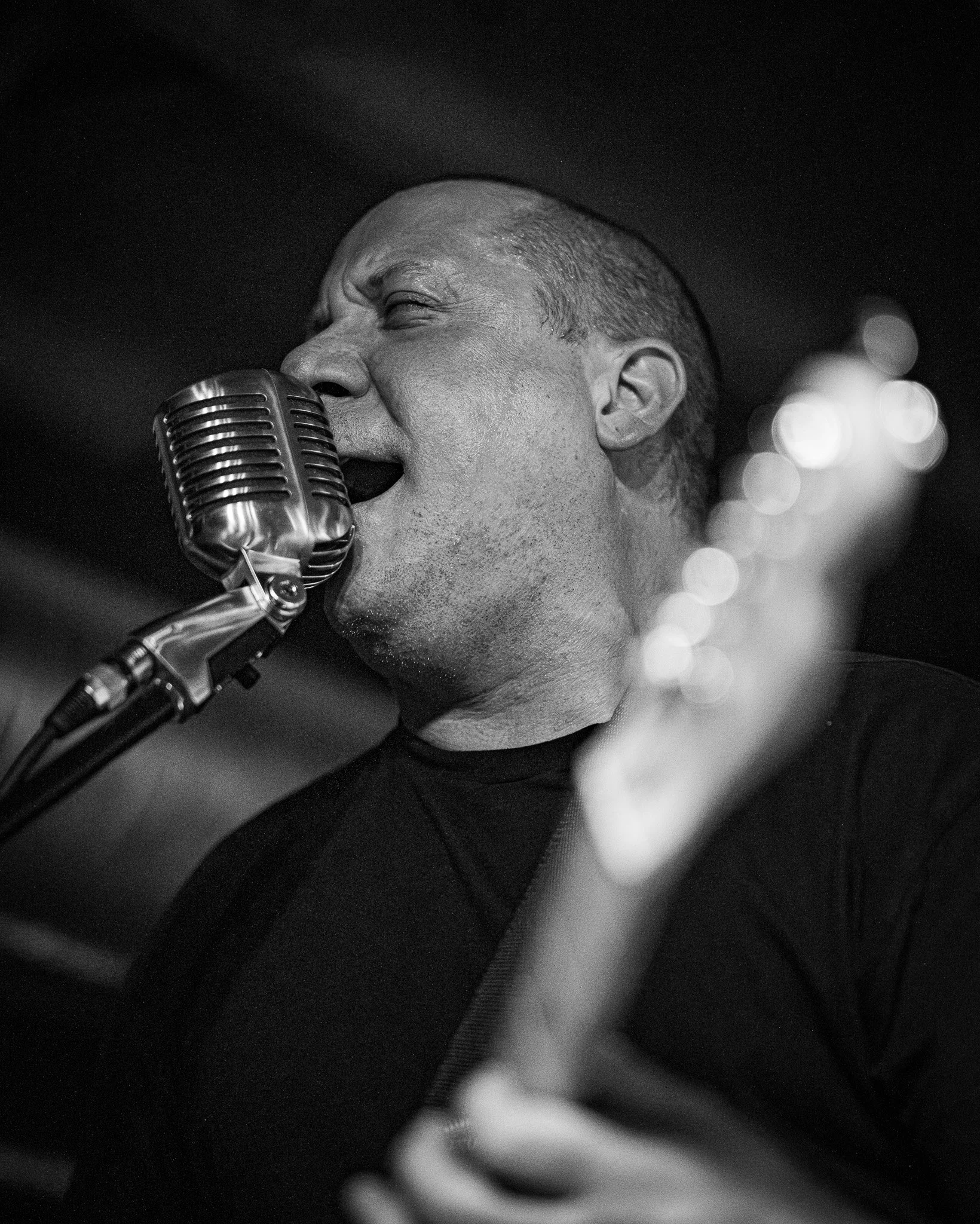 A black and white photo of a man singing passionately into a vintage microphone with his eyes closed and one hand in front of him.