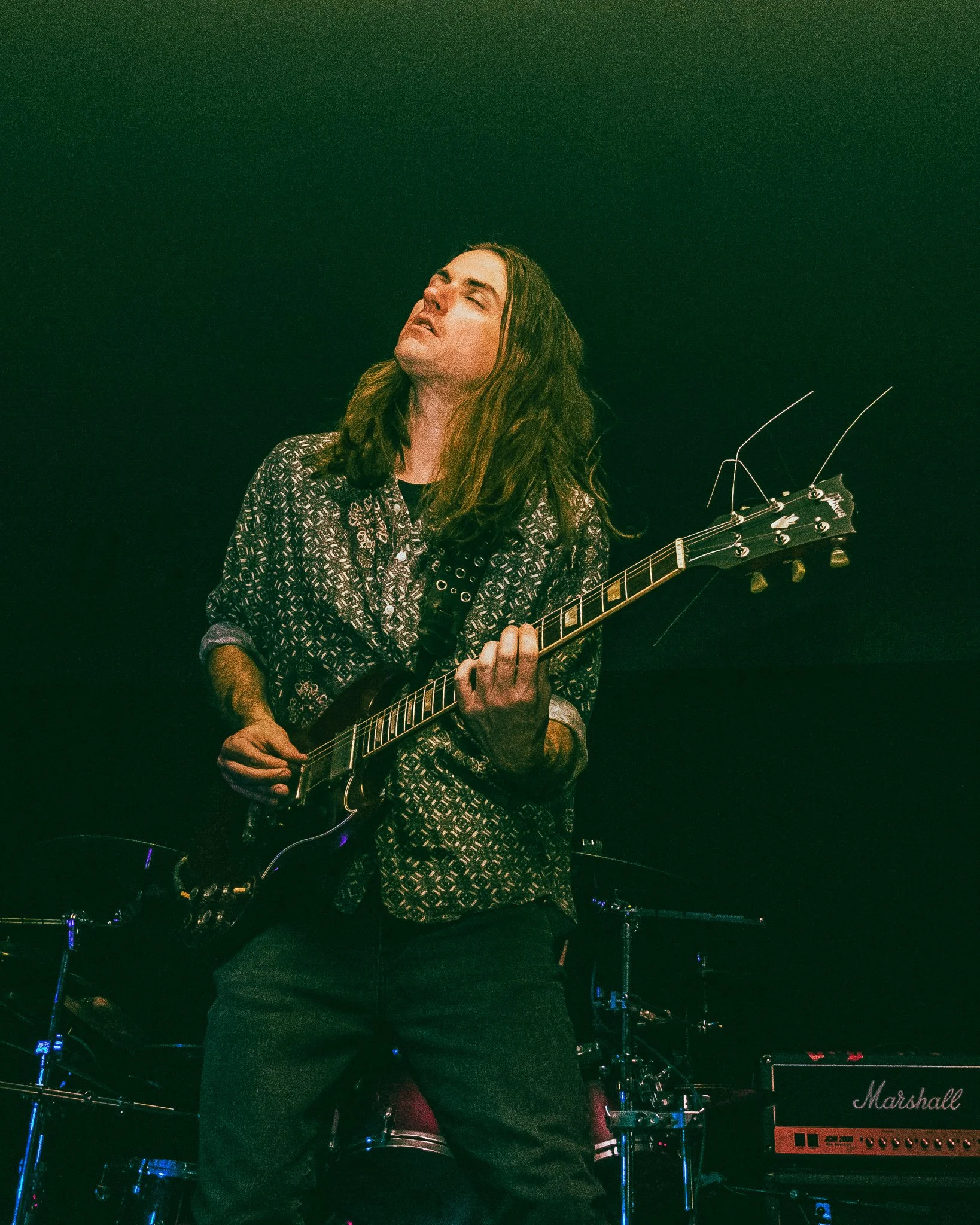 A musician with long hair playing an electric guitar on stage during a concert.