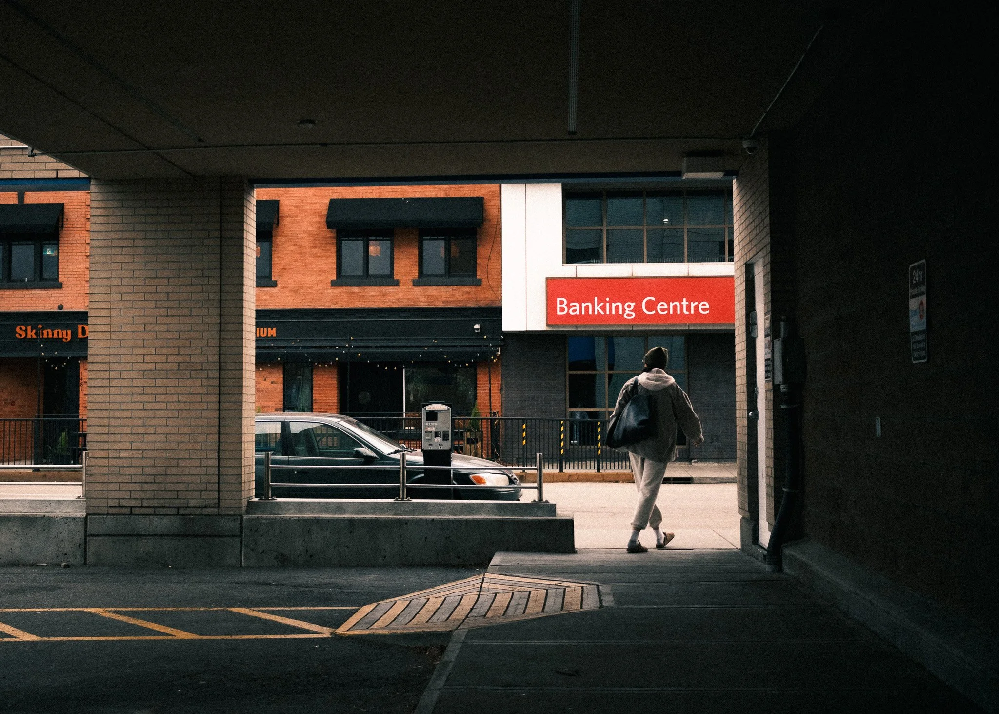Person walking outside a banking center building, view from inside a parking garage.