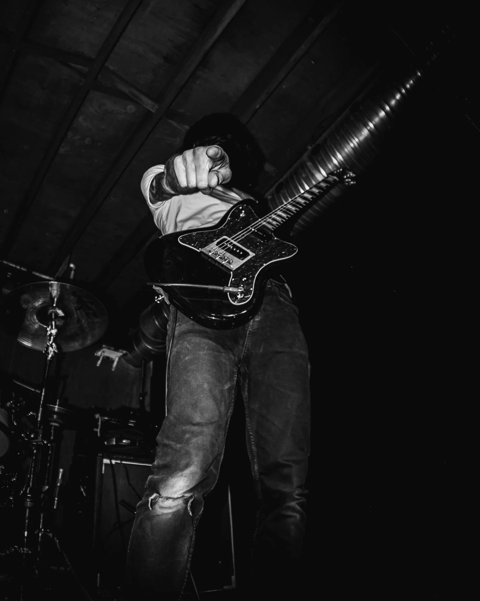 A person pointing towards the camera while playing an electric guitar on stage.