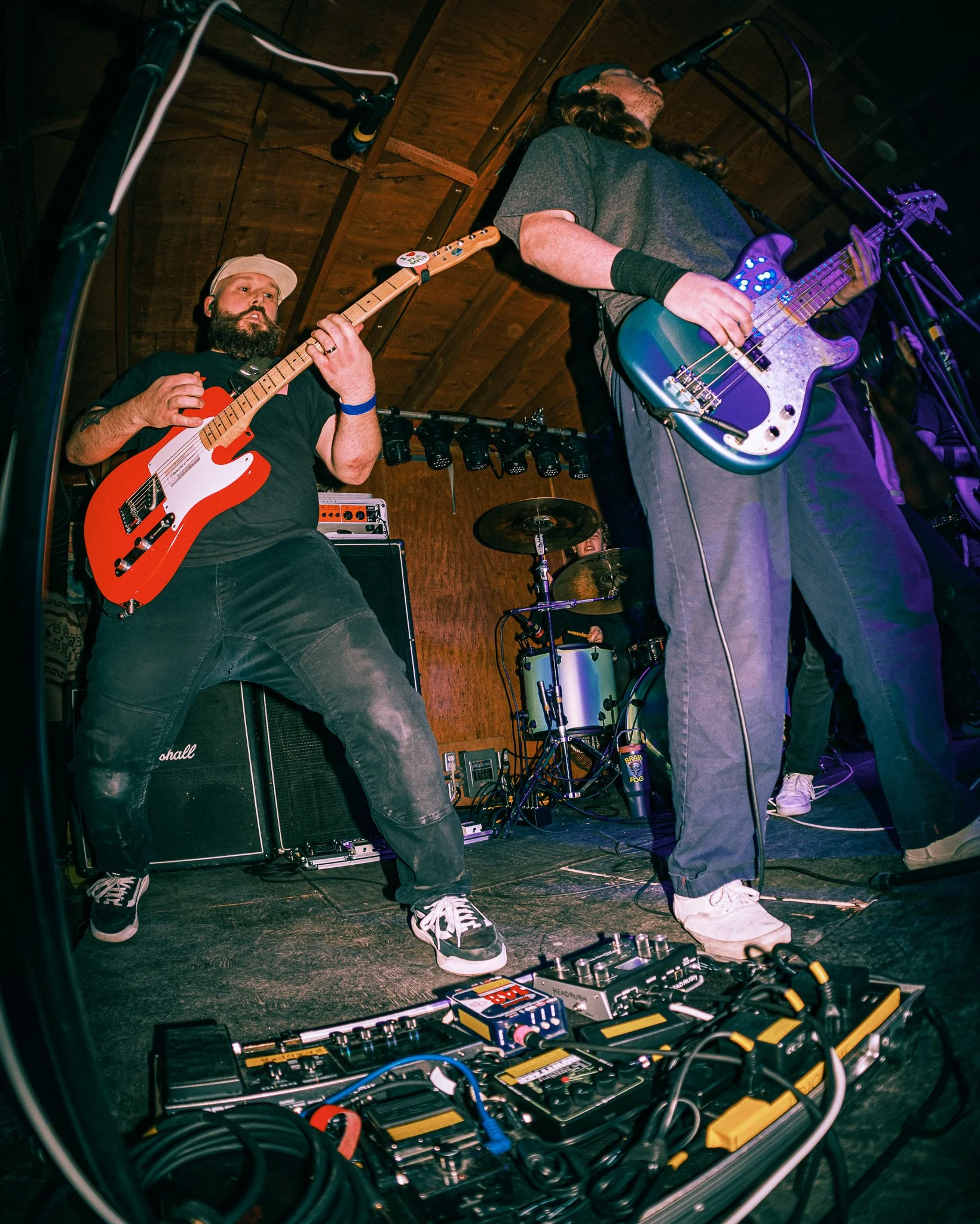 Musicians performing live on stage with guitars and drums in a cozy venue.