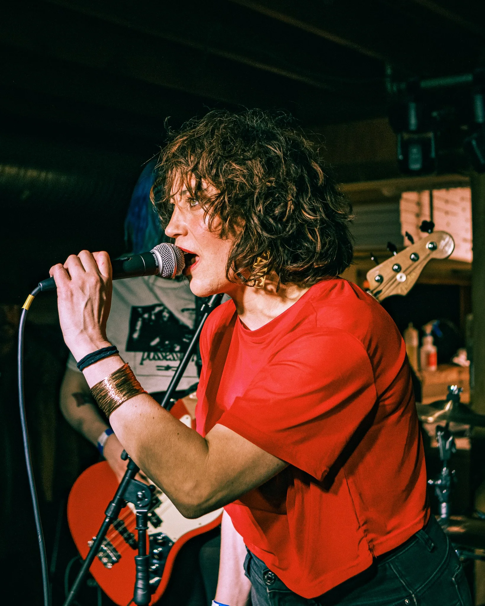 A woman singing into a microphone on stage with a guitar behind her at a music venue.