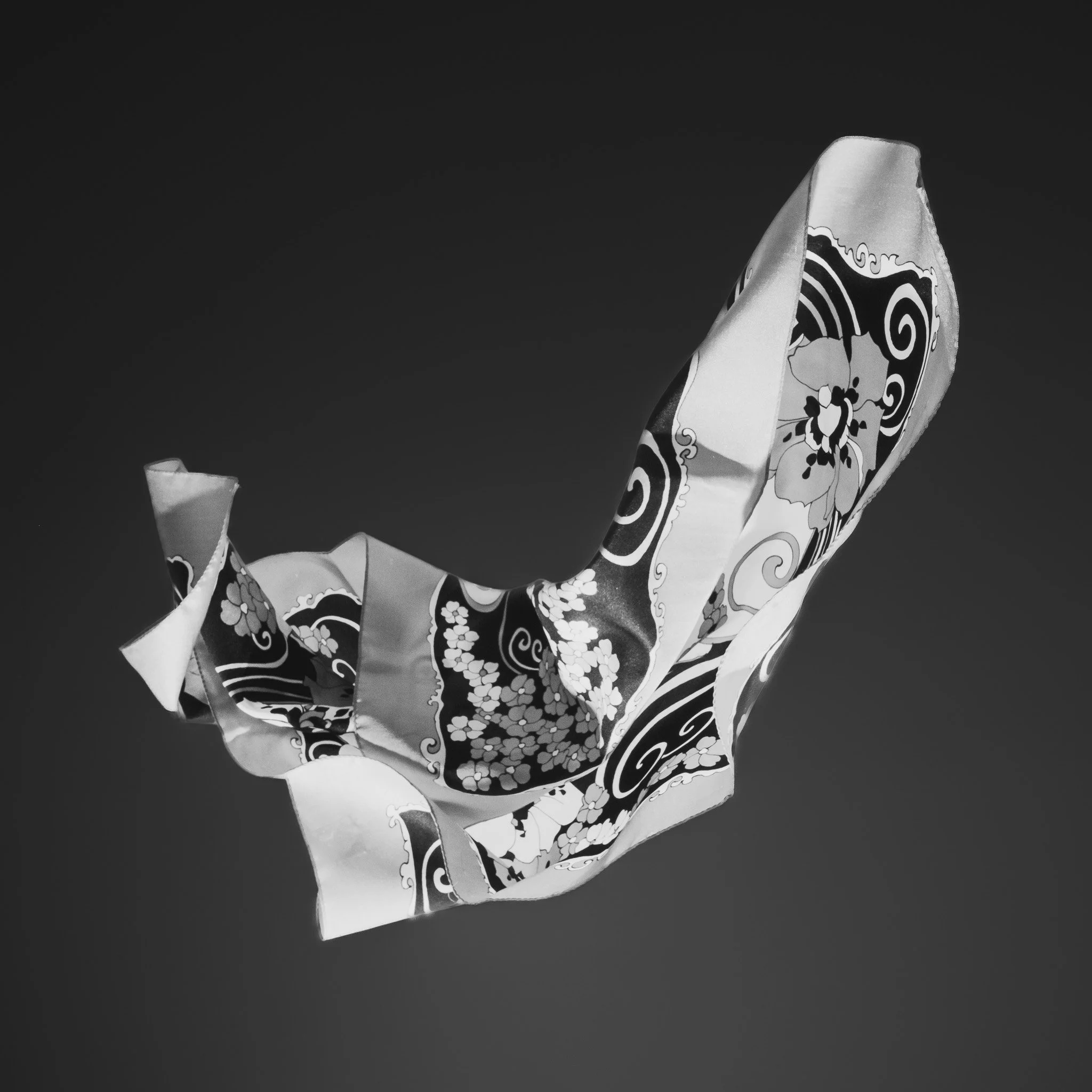 A piece of fabric with floral and swirl designs floating in the air against a dark background.