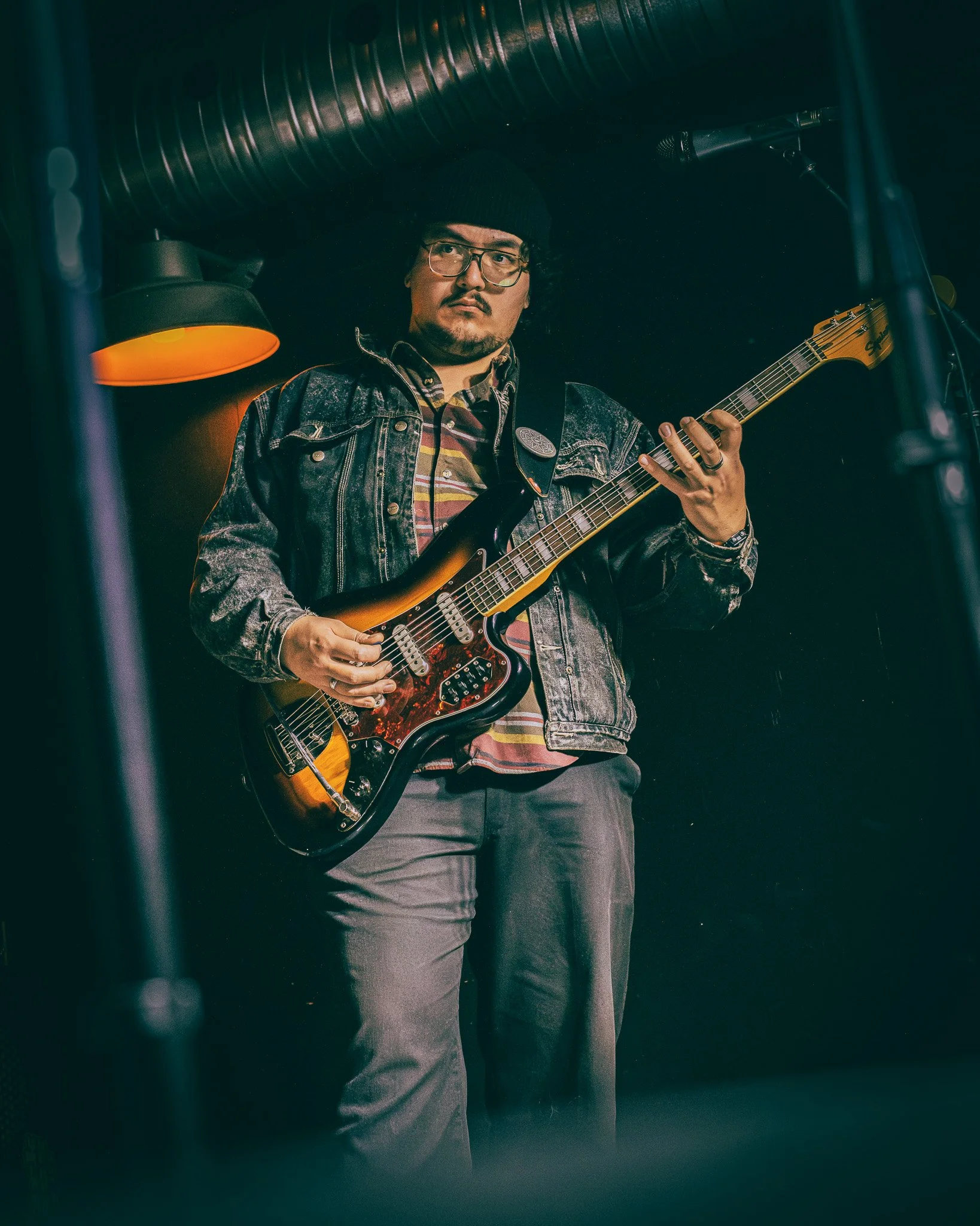 A man playing an electric guitar on a stage with dark background and stage lights.