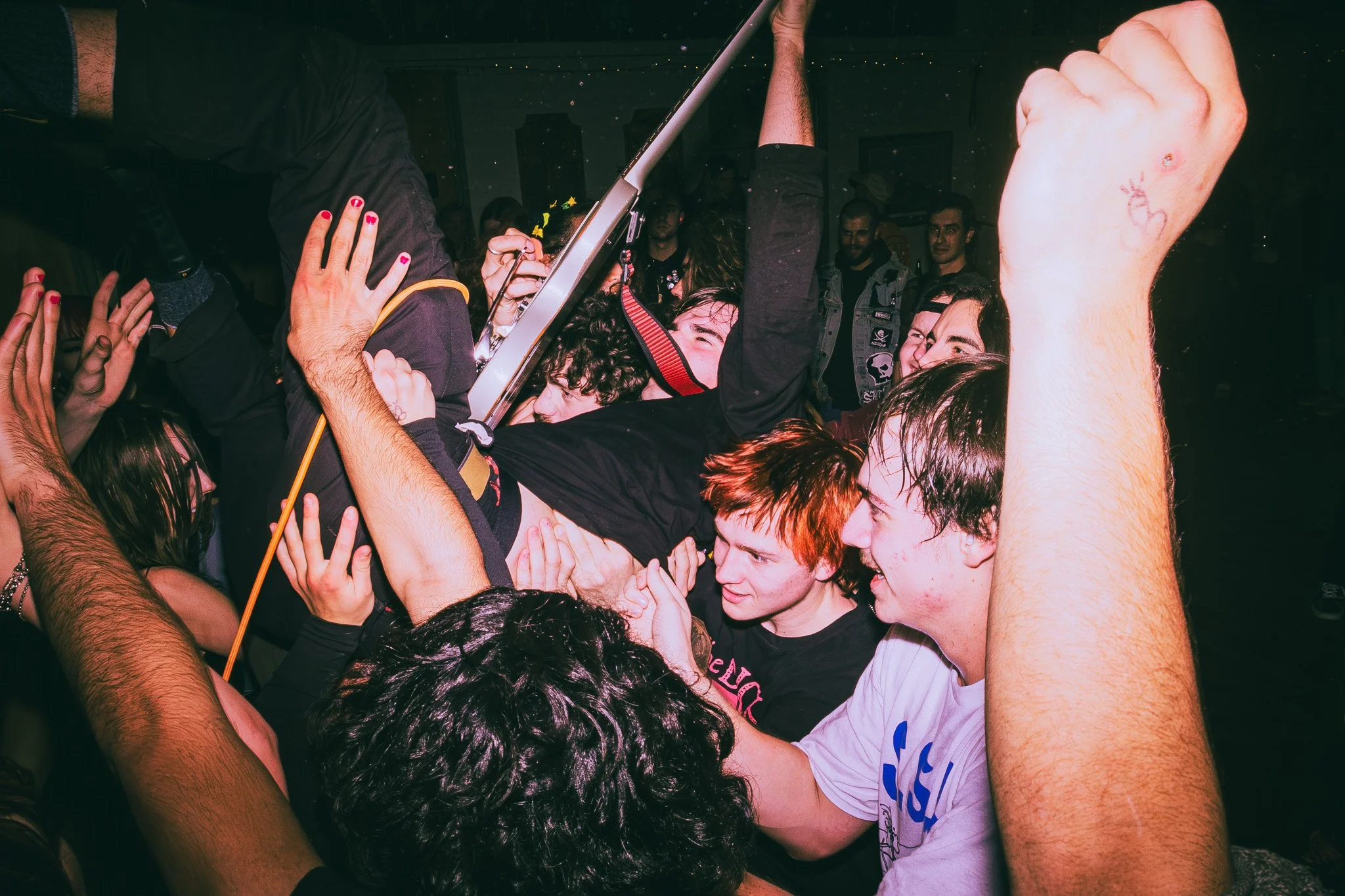 A crowd of people at a concert or event lifting a person in black shirt holding a guitar trophy in the air, all appearing excited and engaged.
