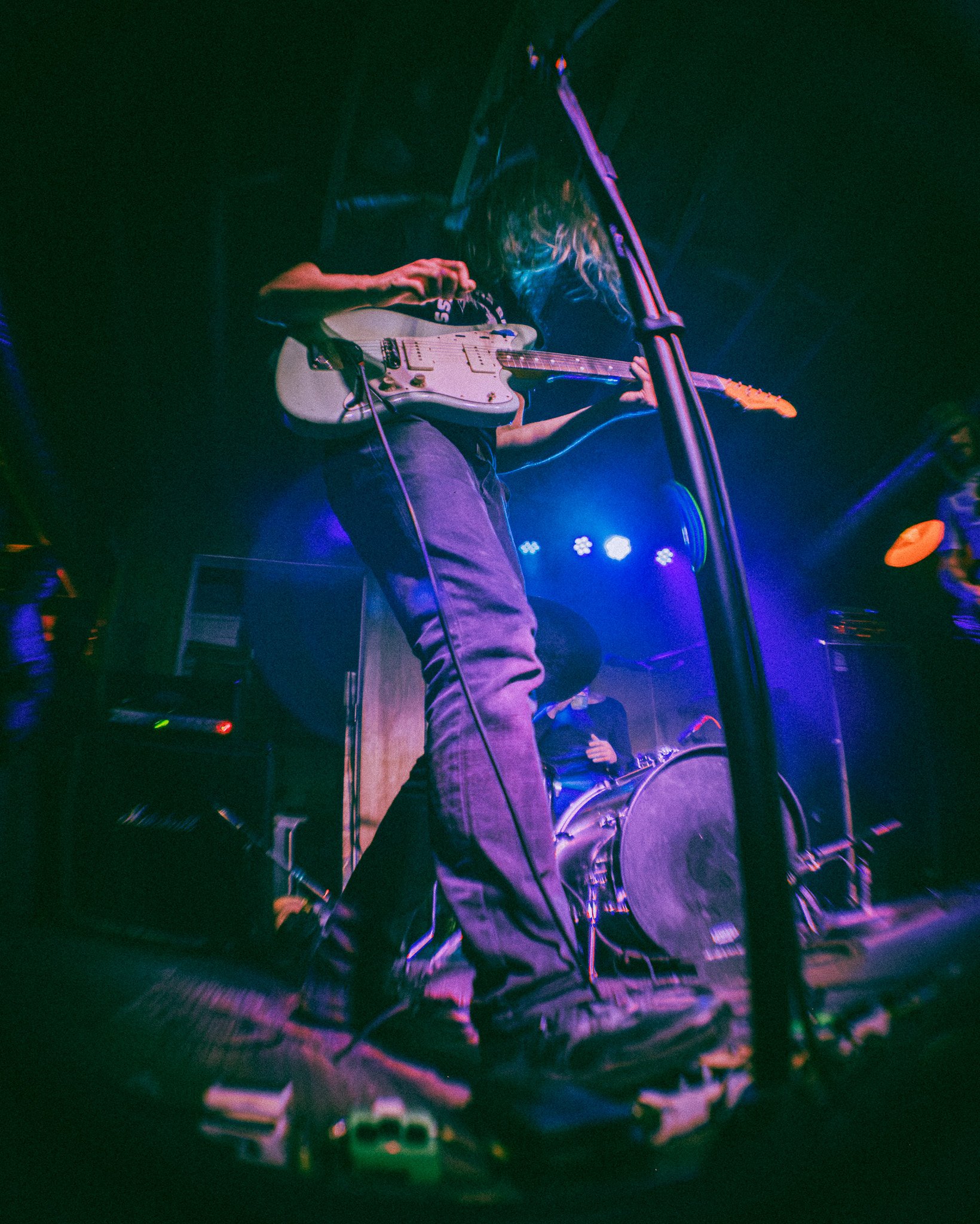 Musician playing electric guitar on a dark stage with colorful lights.