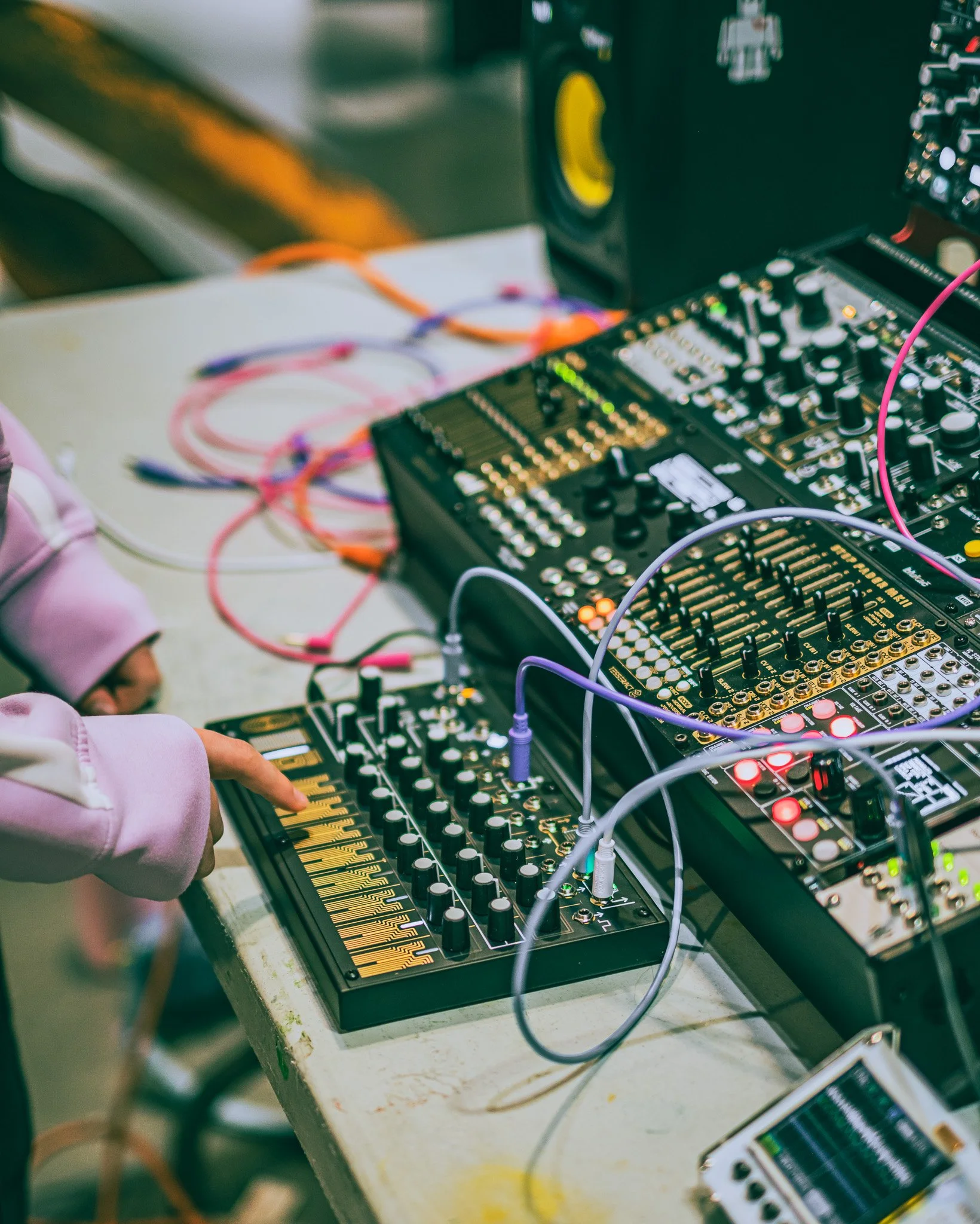 Close-up of a sound mixing console with various knobs, sliders, and cables connected to electronic music equipment.