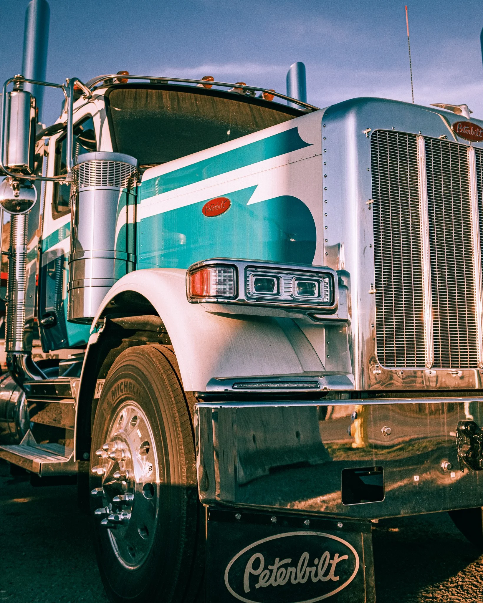 A classic Peterbilt semi-truck with a blue and white color scheme and chrome accents, parked outdoors with a clear sky.