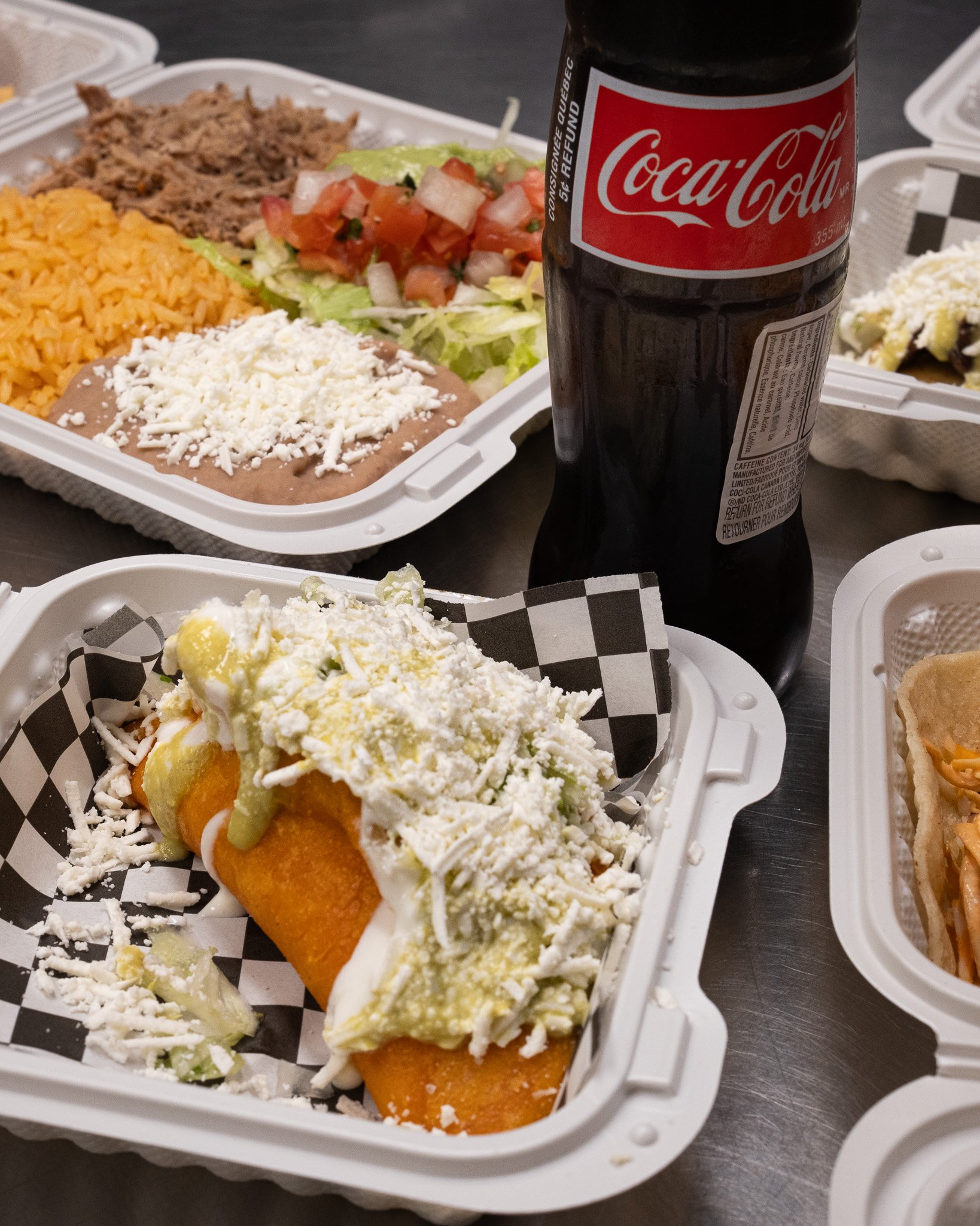 Takeout Mexican food with a Coca-Cola bottle on a table.