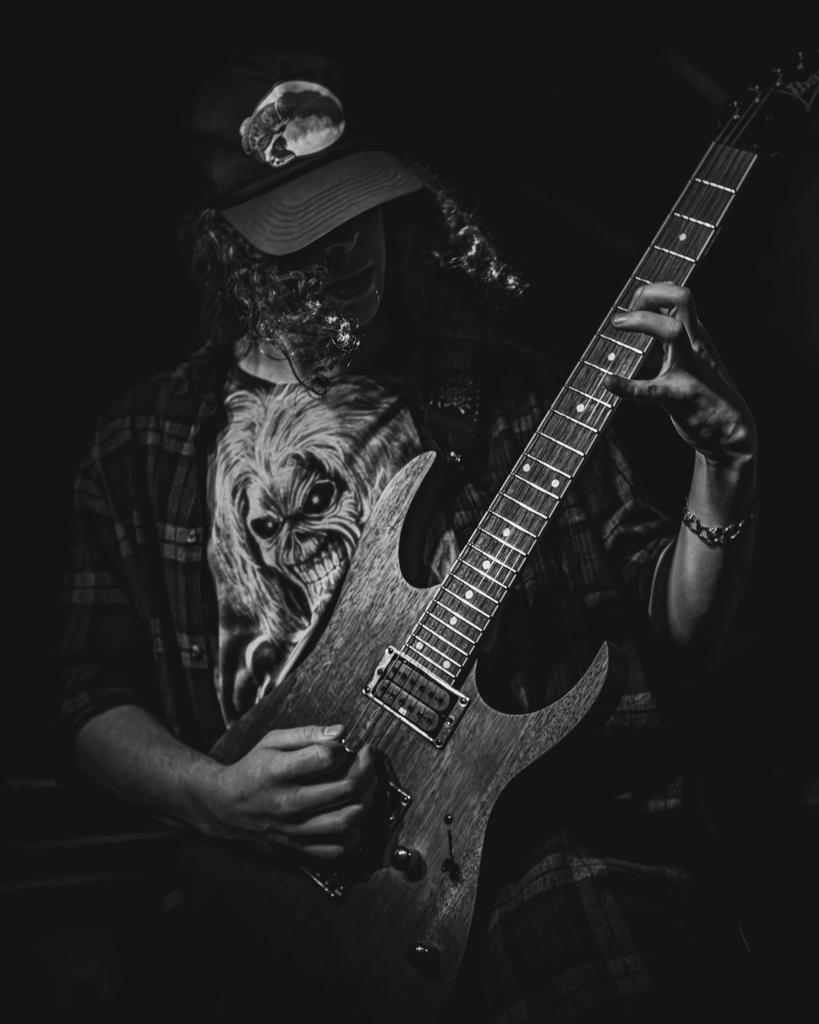 A person playing an electric guitar in a dark setting, wearing a cap and a T-shirt with a skull design.