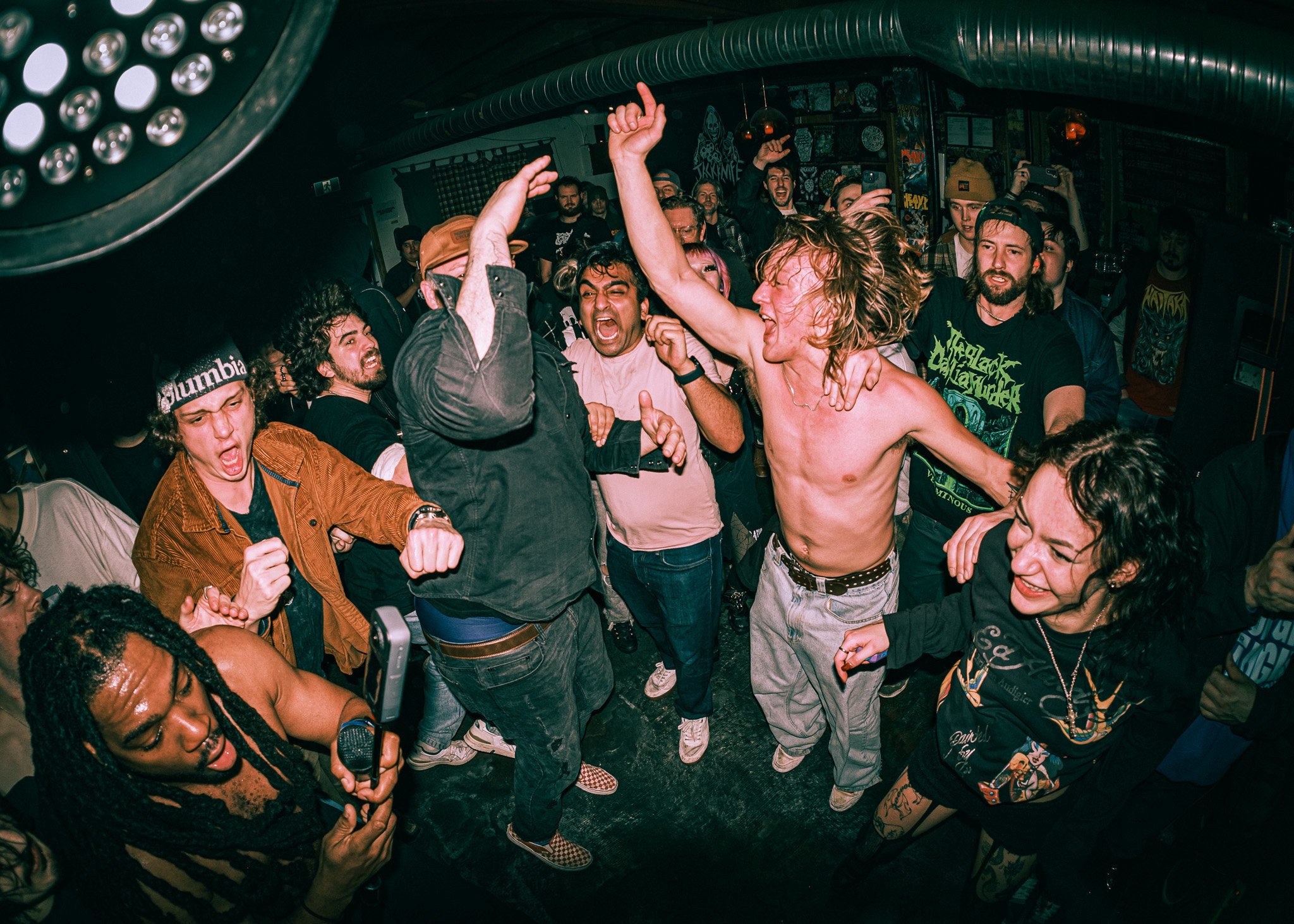 People dancing and enjoying music at a concert or nightclub, with some individuals singing, raising their hands, and smiling.