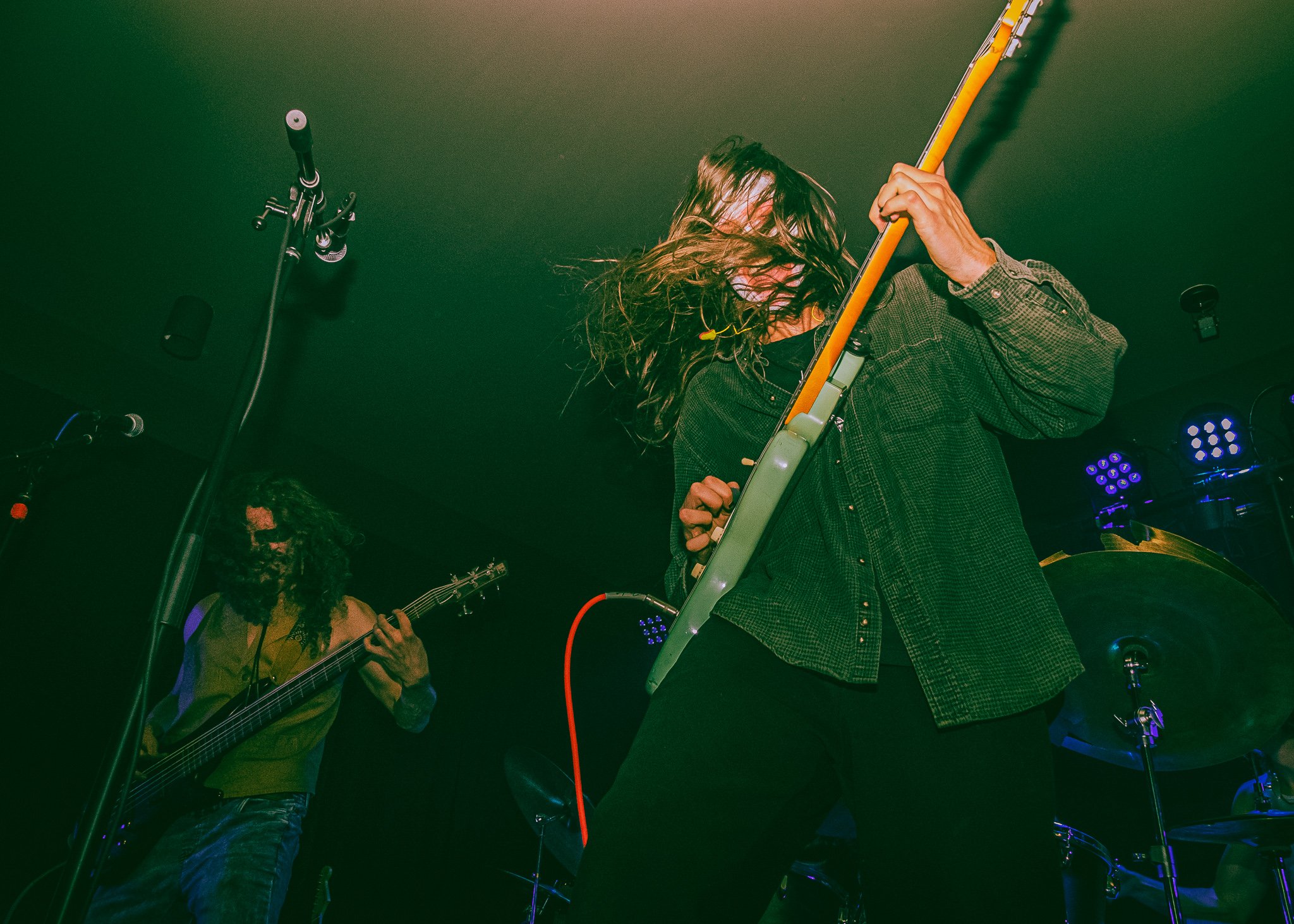 Musicians performing live on stage, one playing guitar and the other playing bass, with colorful stage lights