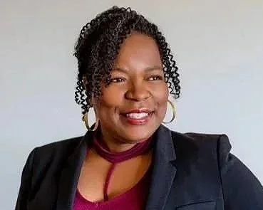 Black woman with curly hair wearing dark blazer, smiling