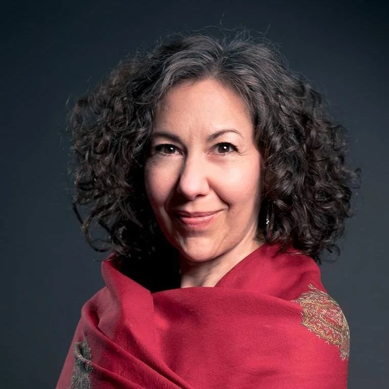 White woman with curly gray hair wearing red shawl, smiling softly