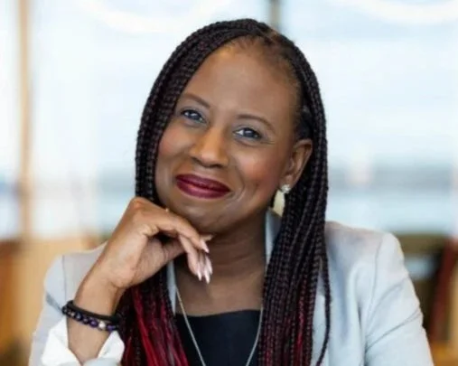 Black woman with braided hair wearing light blazer, smiling warmly