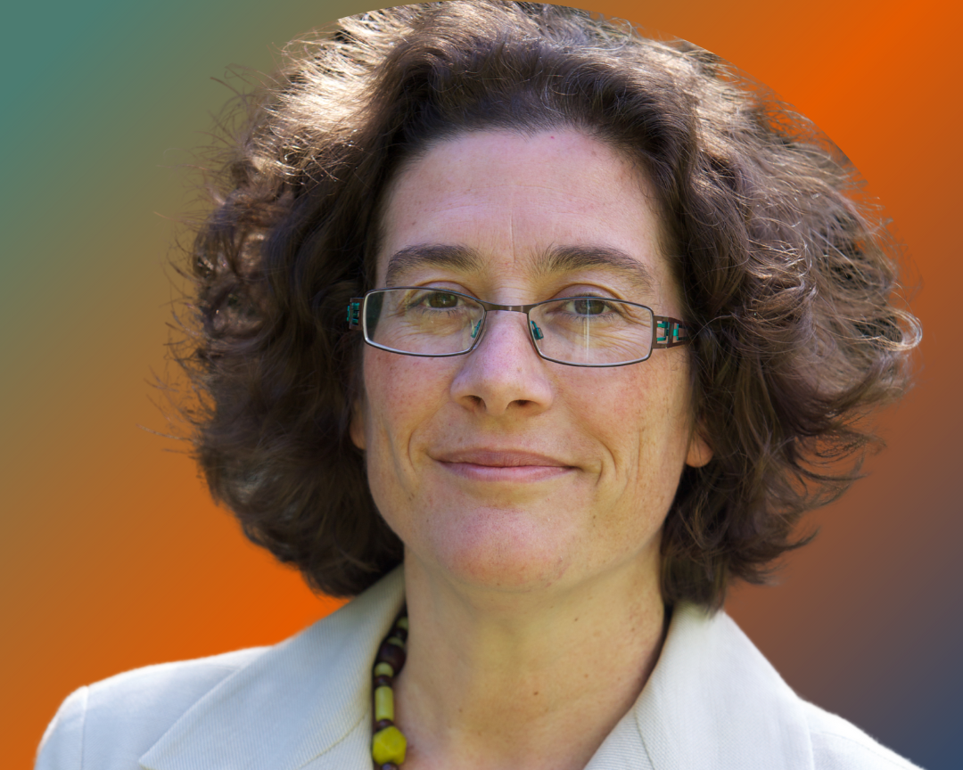Woman with curly brown hair and glasses wearing light blazer, photographed outdoors