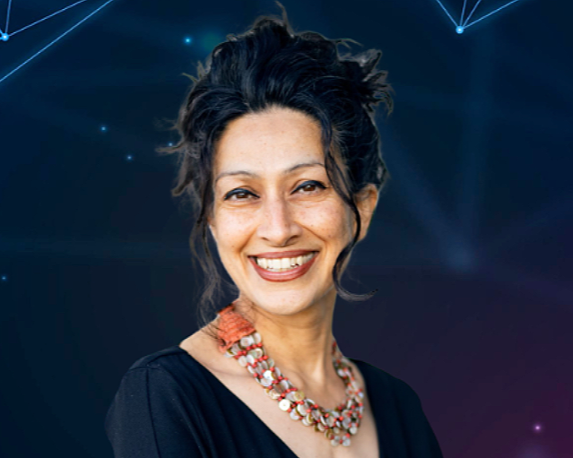 A South Asian woman smiling, photographed against digital light display