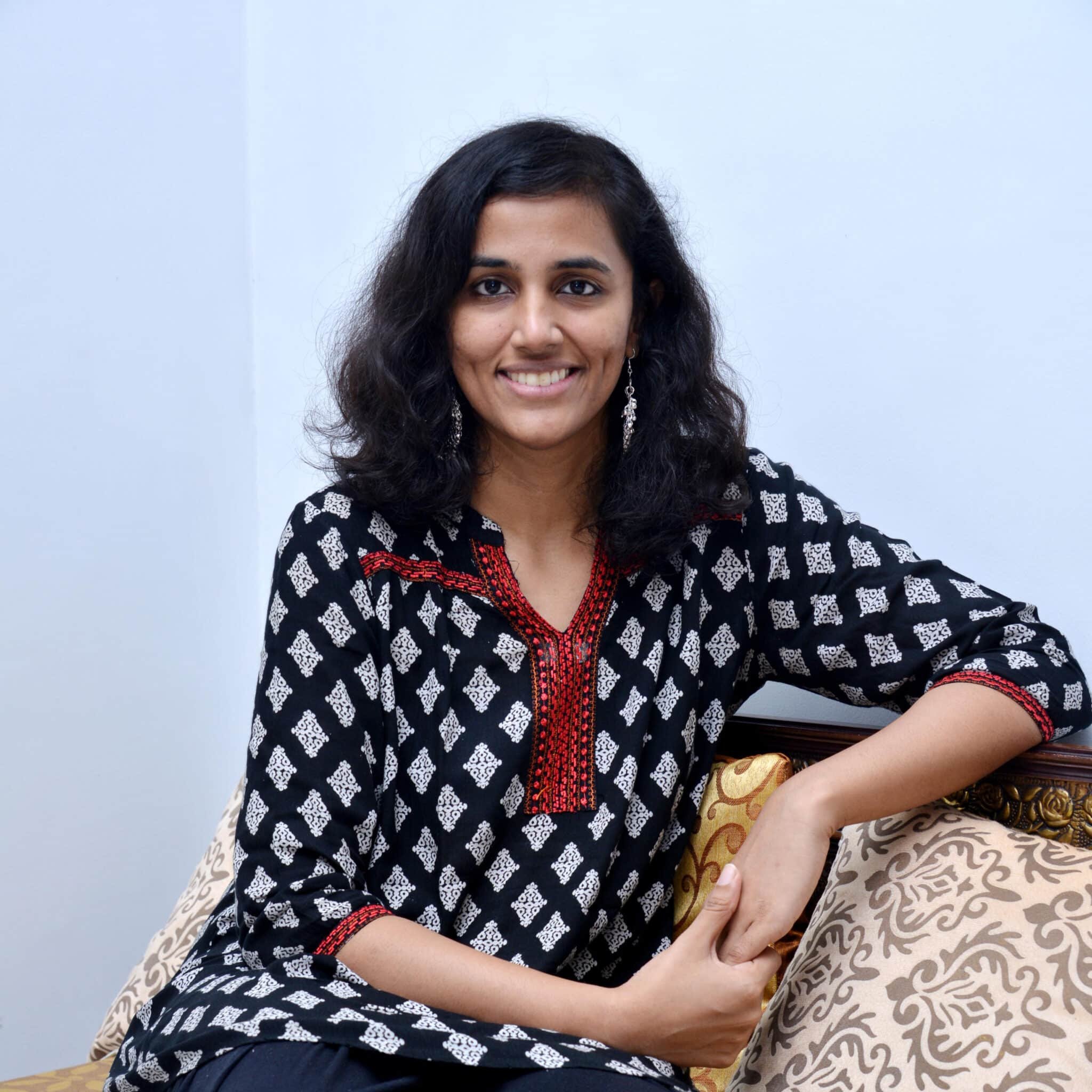 South Asian woman wearing black kurta with white and red embroidery, seated and smiling