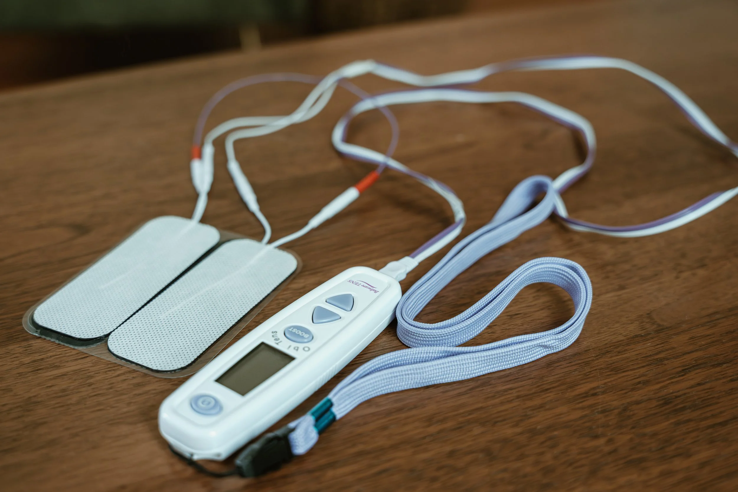 A TENS unit, with pads, wires, and a digital control for labour and pregnancy pain relief, placed on a wooden surface.