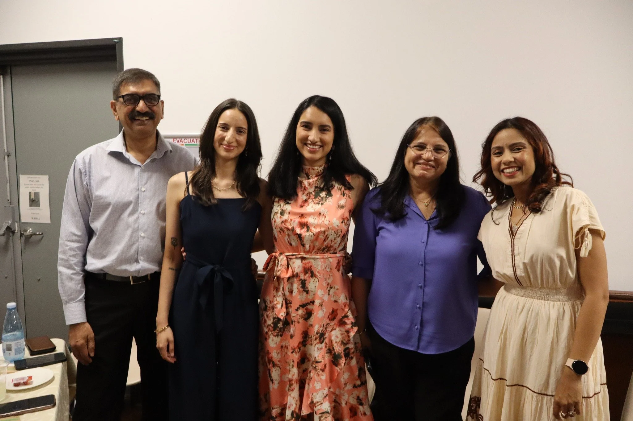 Group of five diverse women and one man standing together indoors, smiling at the camera.