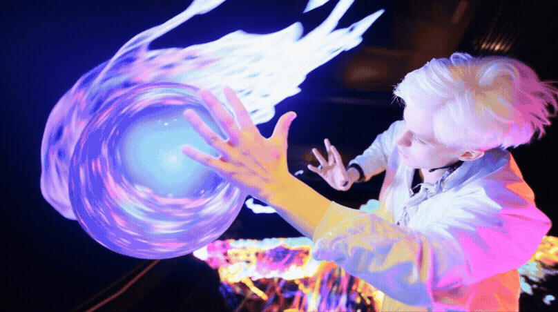 A person with platinum blonde hair in a white jacket creates a swirling, glowing, colorful digital or virtual energy vortex.