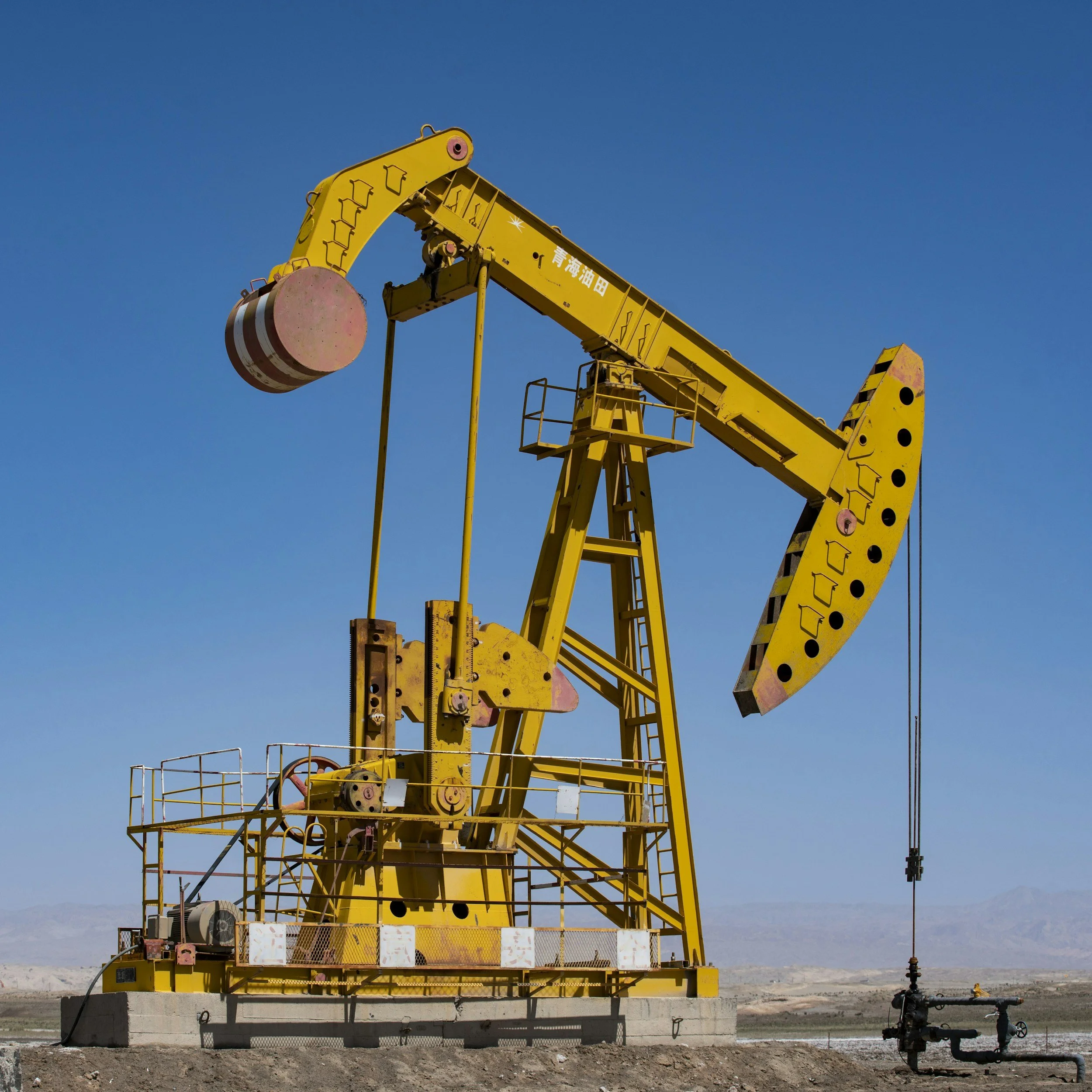 Yellow oil pumpjack operating in a desert landscape under a clear blue sky.
