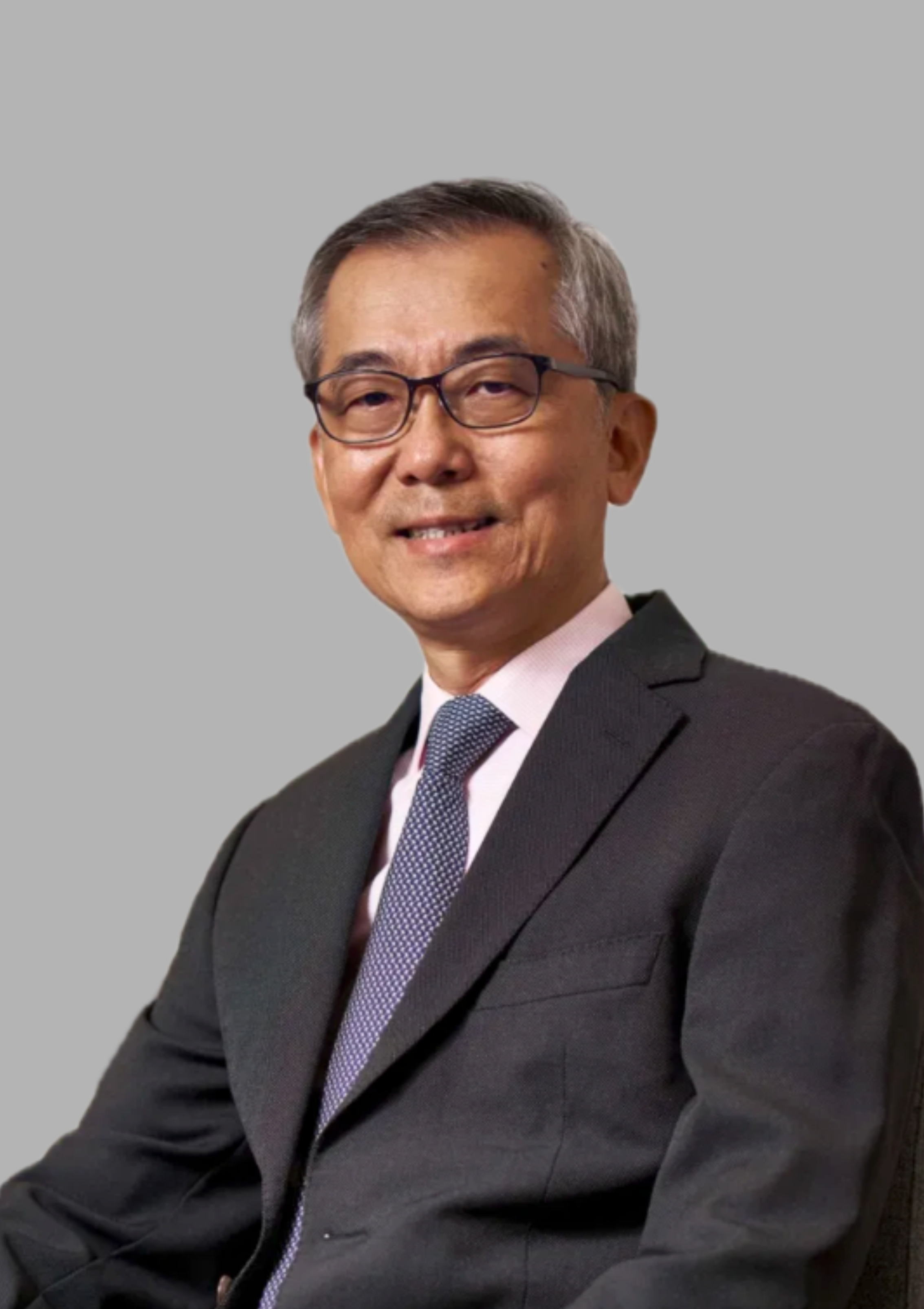 Portrait of a middle-aged man with glasses, wearing a dark suit, white shirt, and patterned tie, smiling against a plain gray background.
